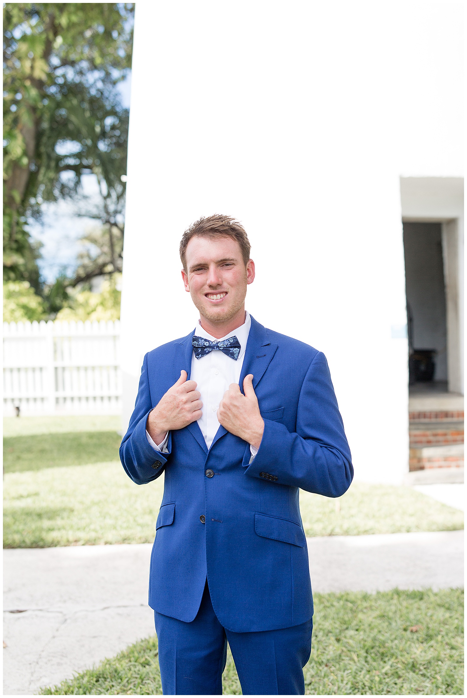 groom holding edges of blue suit with blue bowtie smiling by lighthouse at hemingway house