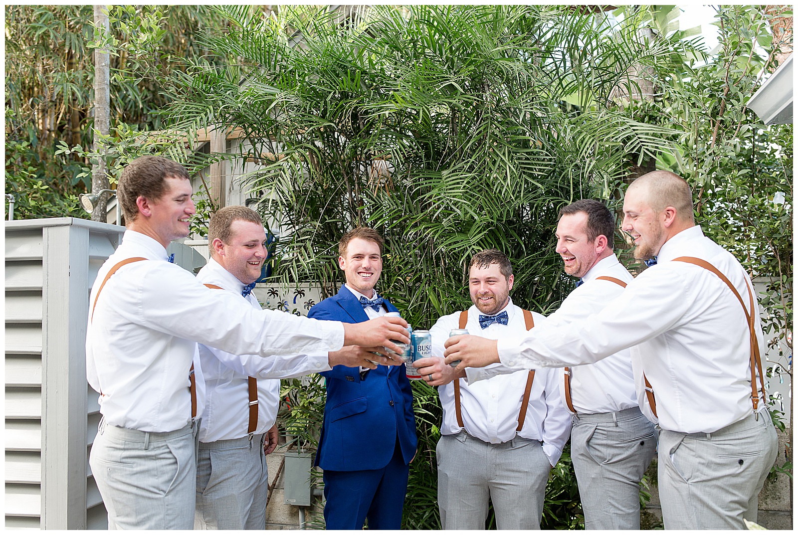 groom with five groomsmen in white shirts with suspenders and light gray pants toasting and smiling at hemingway house