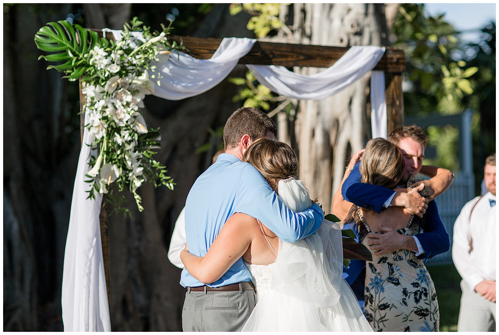 bride and groom hugging guests after ceremony with linen draped archway in background at hemingway house 