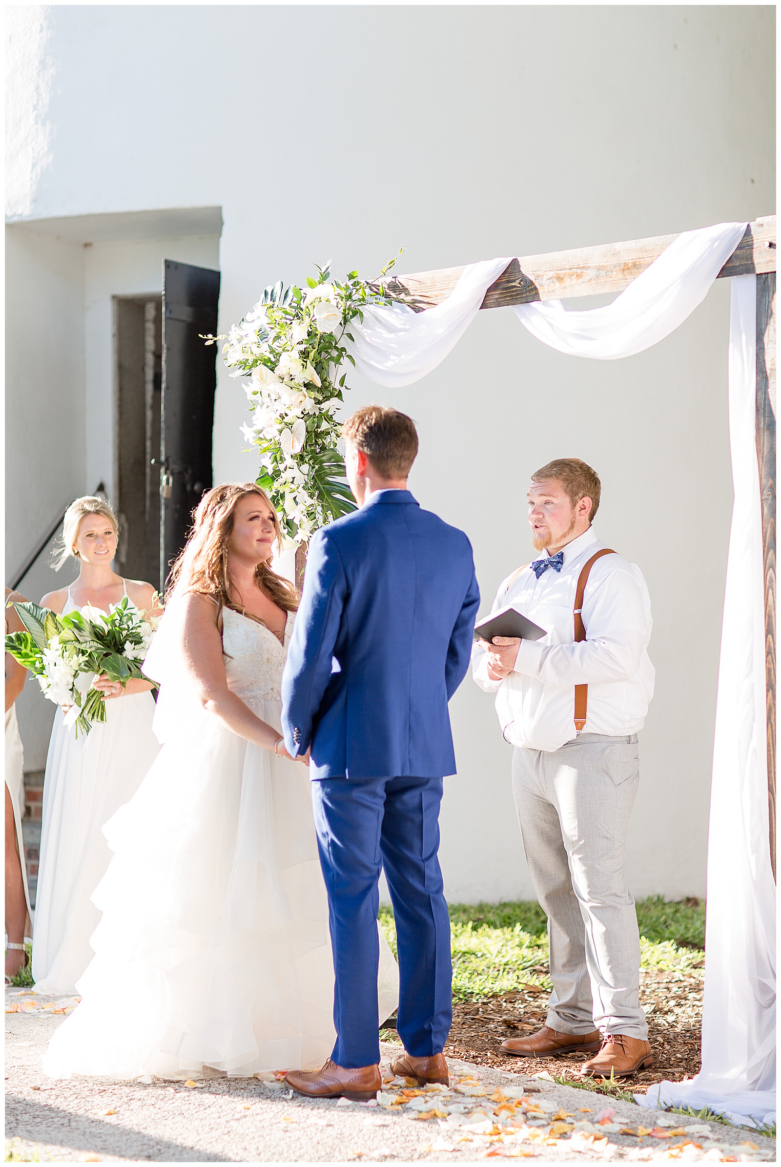 bride and groom saying their vows on sunny day by white lighthouse with bridesmaid and groomsman nearby in key west florida