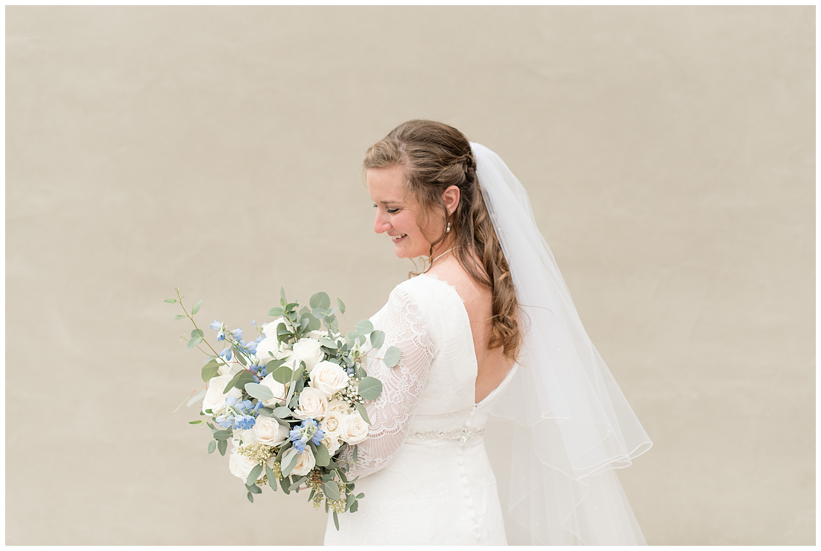 bride smiles looking down at her bridal bouquet of pastel blue and white flowers on her wedding day