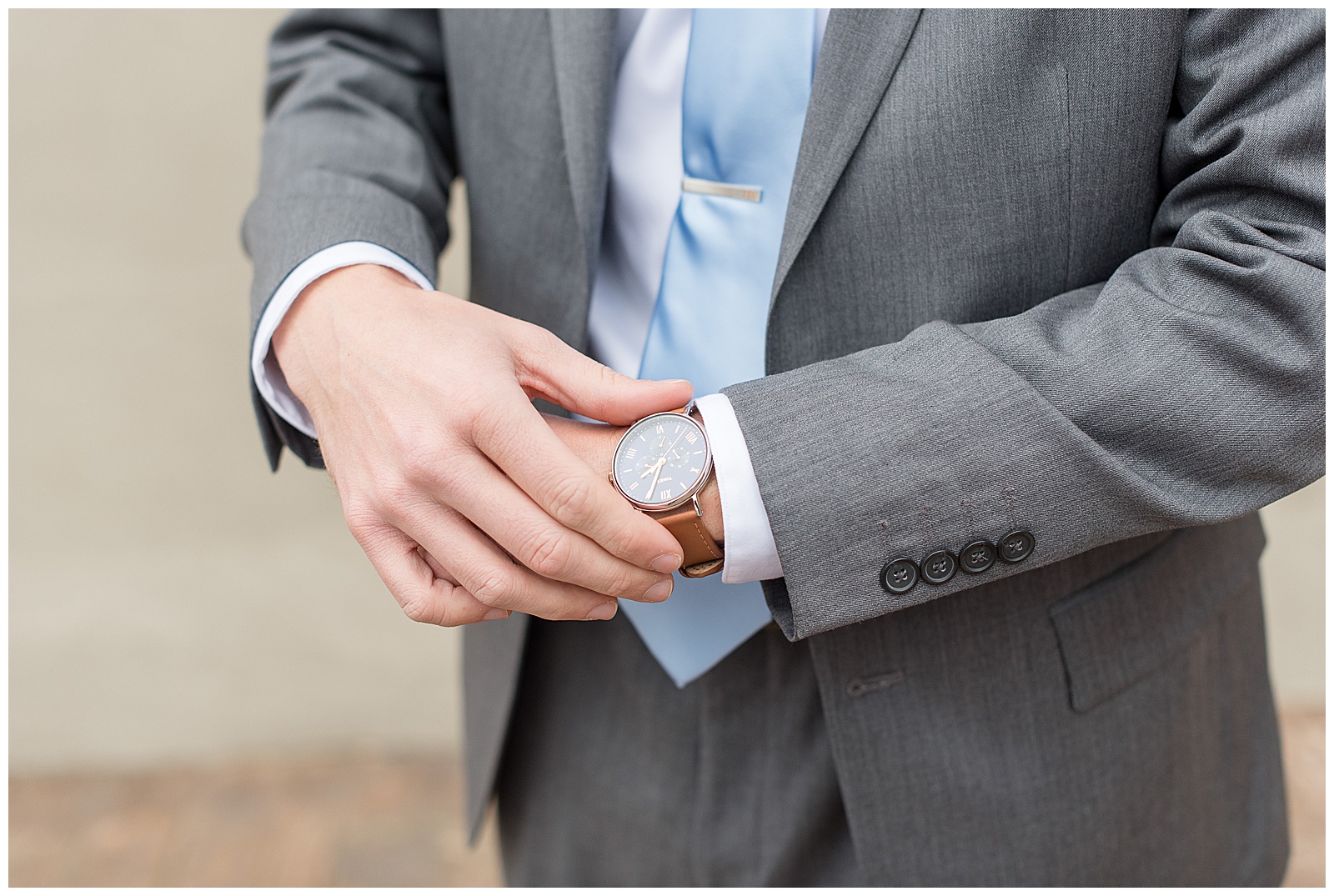 close up of groom in gray suit with baby blue tie displaying his watch on his wrist