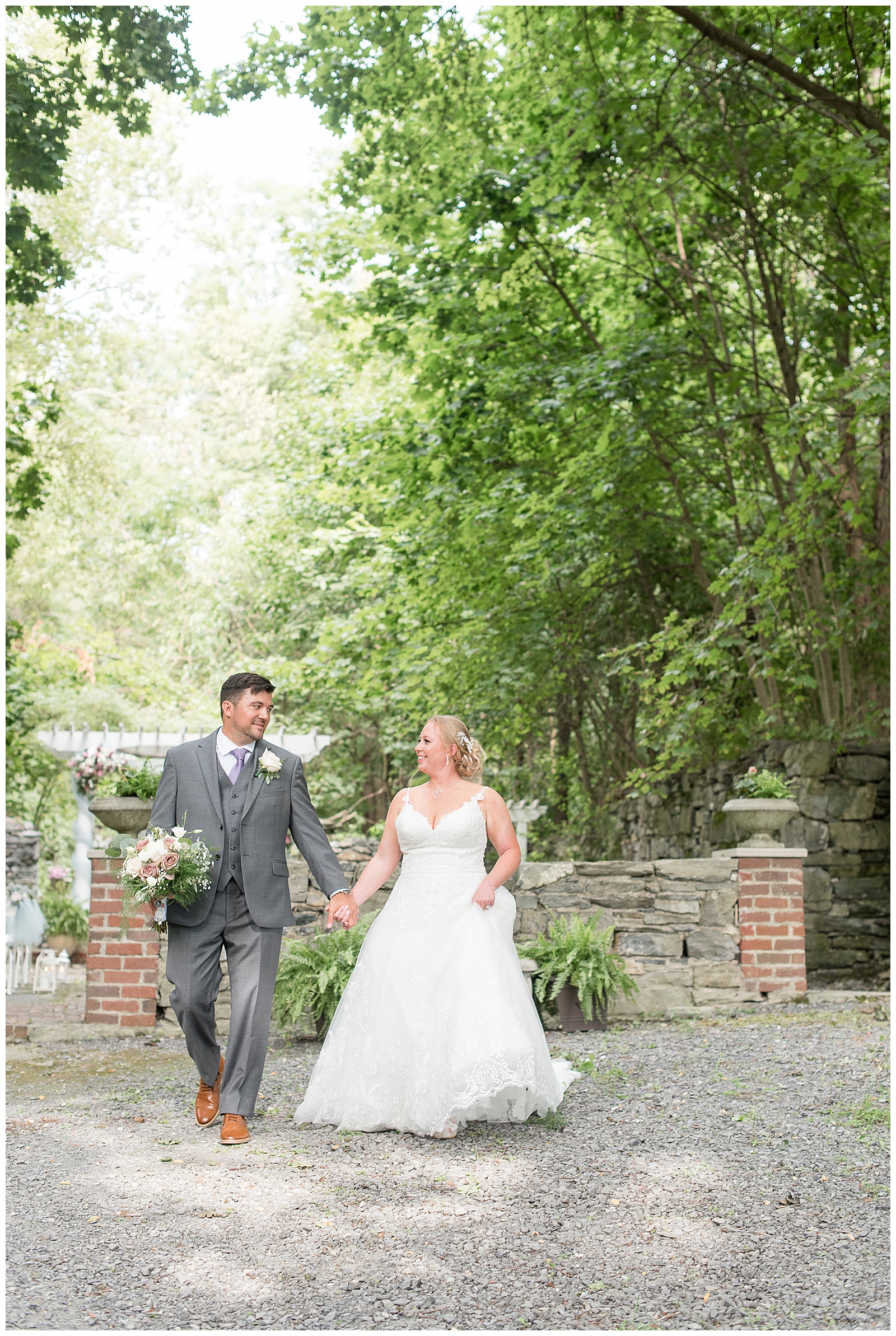 groom and bride holding hands as groom holds bouquet as they walk on stone path at fallen tree farms