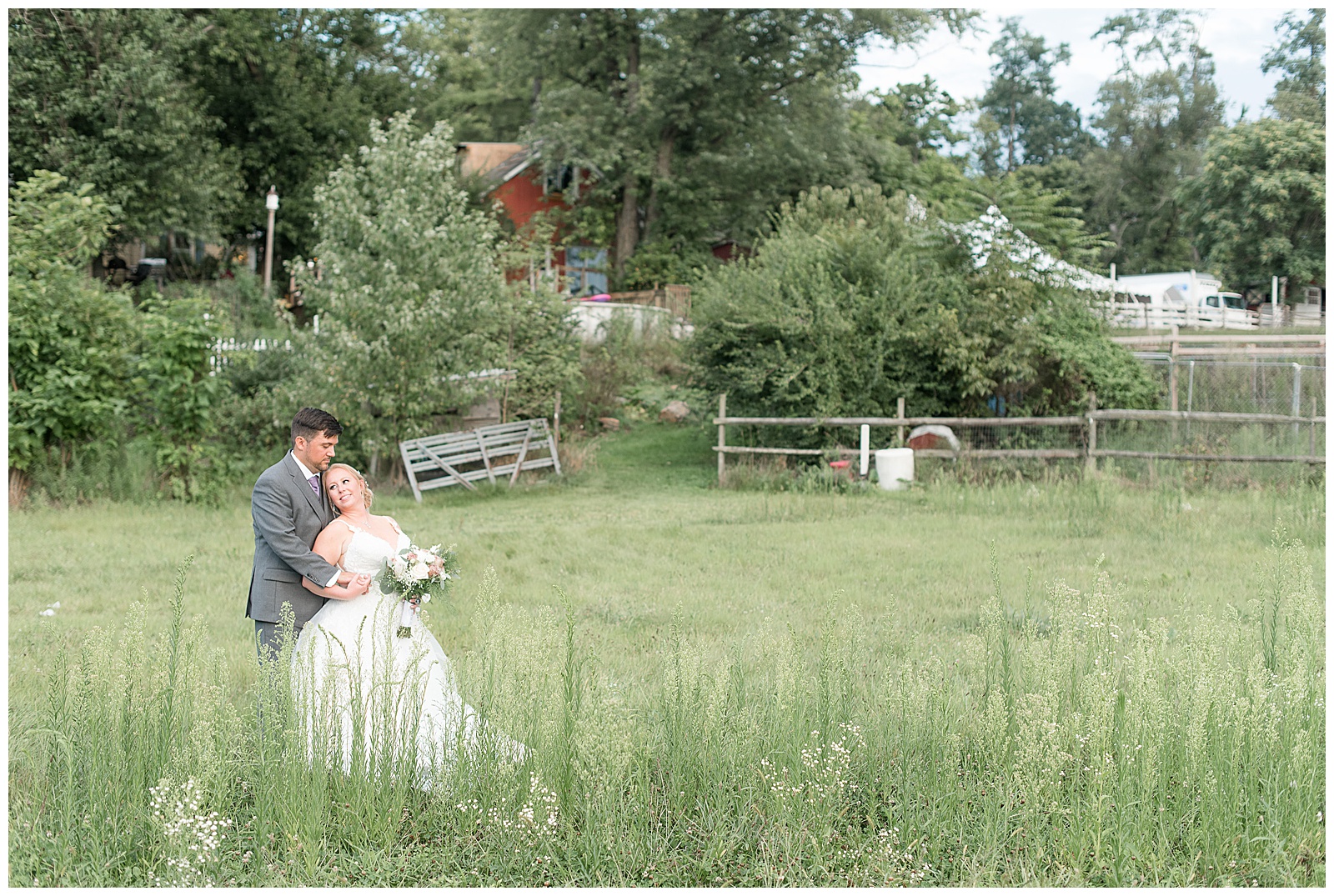 groom hugs bride as she leans back against him in grassy field at fallen tree farm bed and breakfast