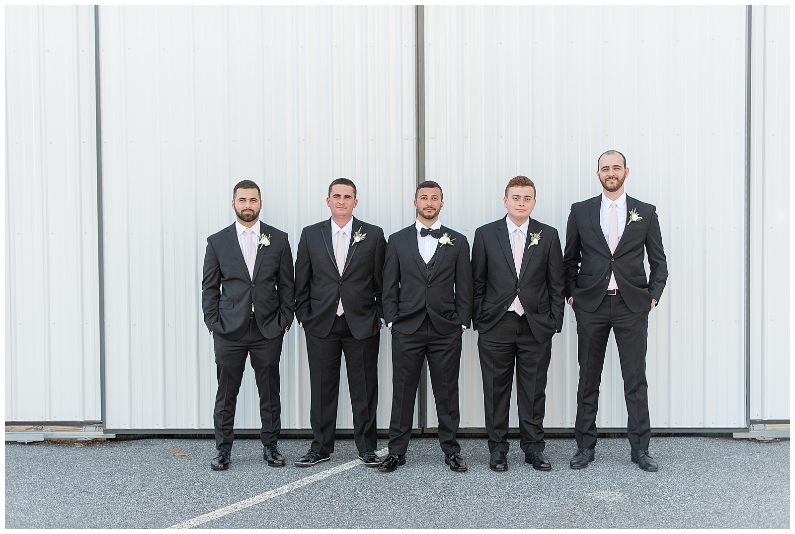 groom and his four groomsmen all with their hands in their pockets smiling at camera along white barn door