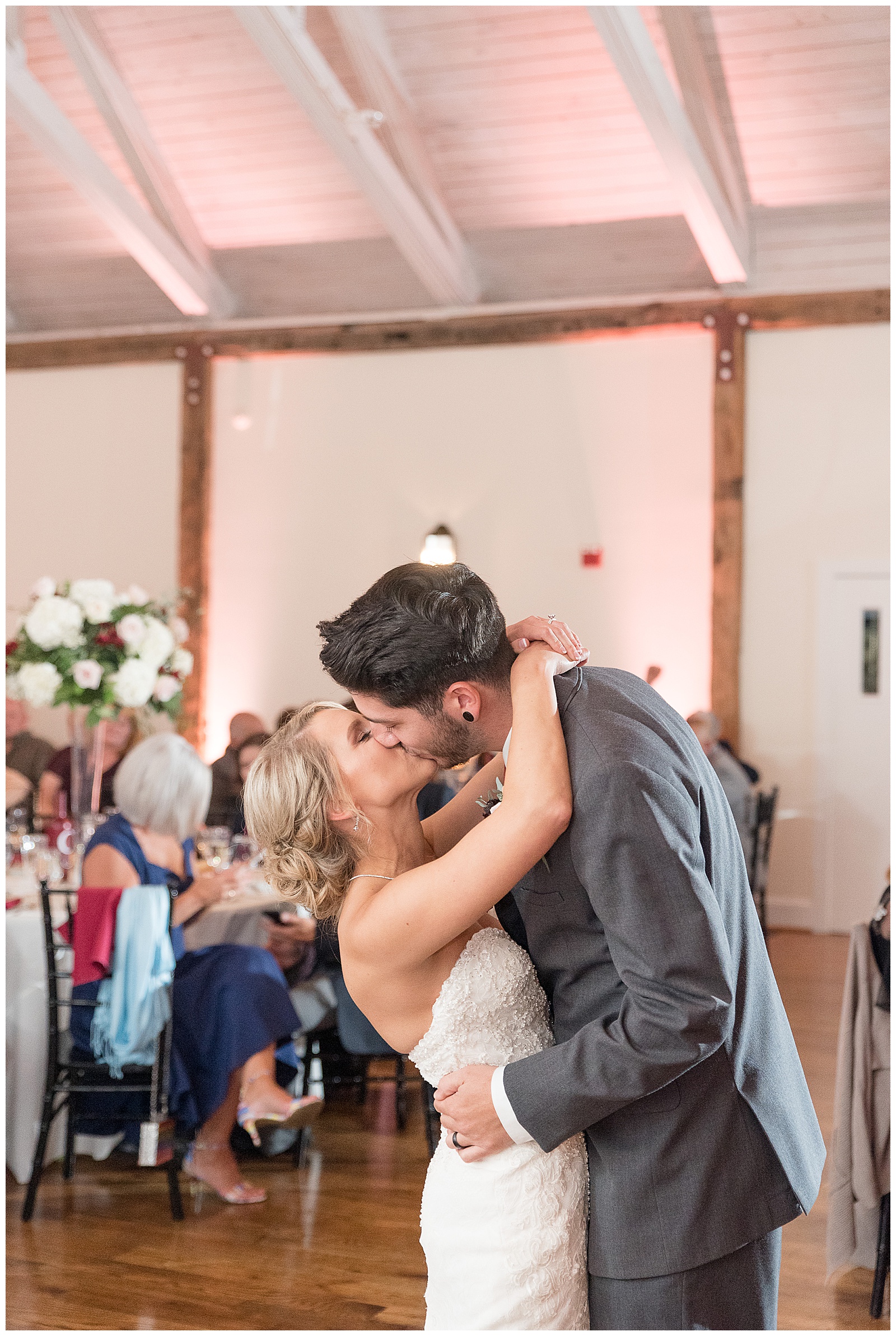 groom slightly dipping bride back as they kiss during during their first dance at reception surrounded by guests