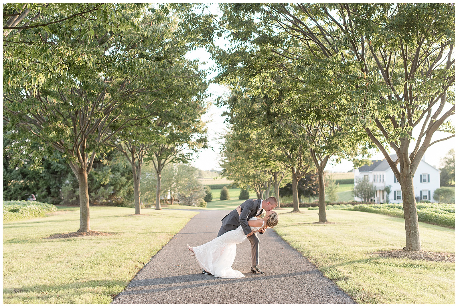groom dips bride back kissing her along paved treelined path at lakefield weddings