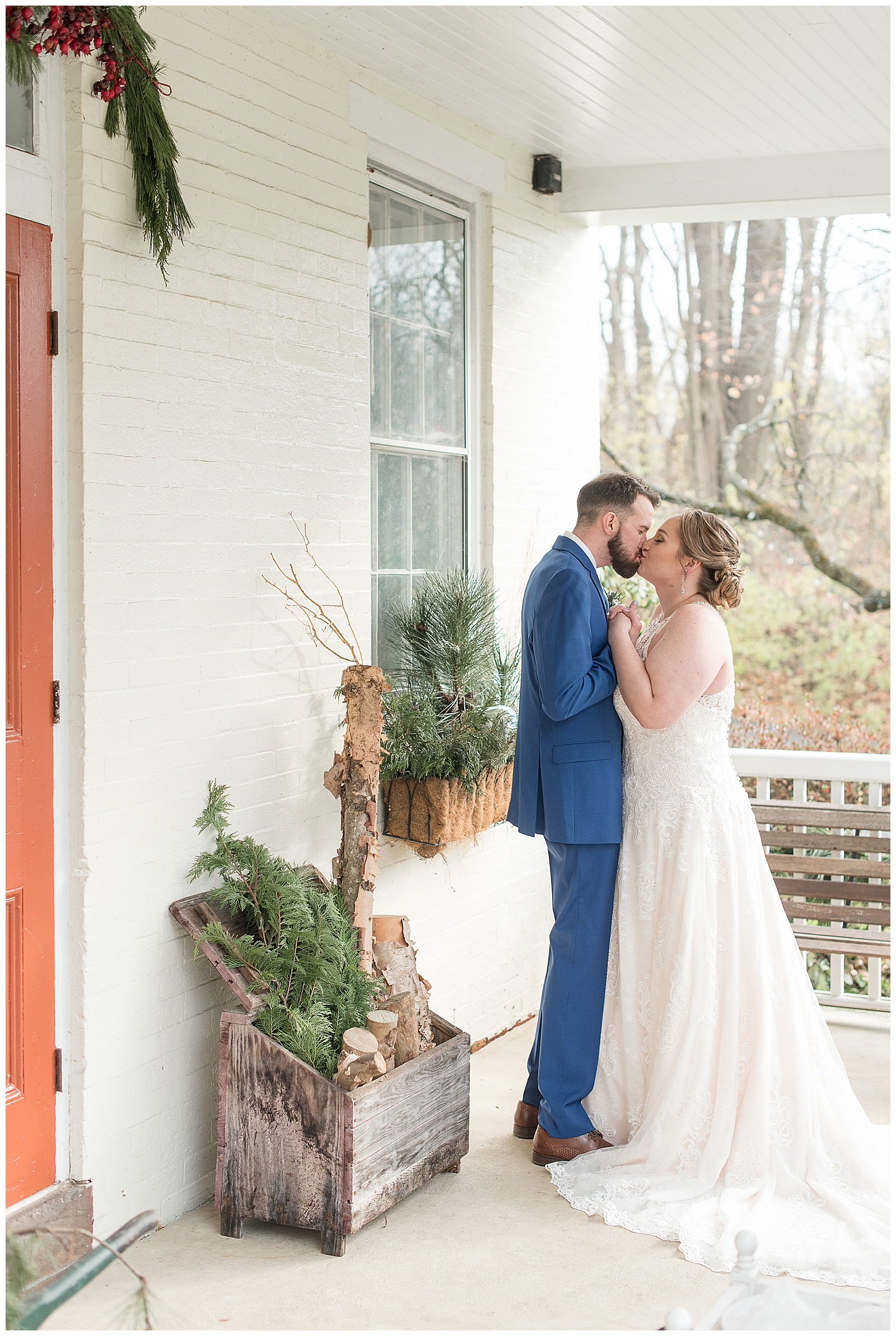 bride and groom kissing on front porch white home with winter greens and wood displayed