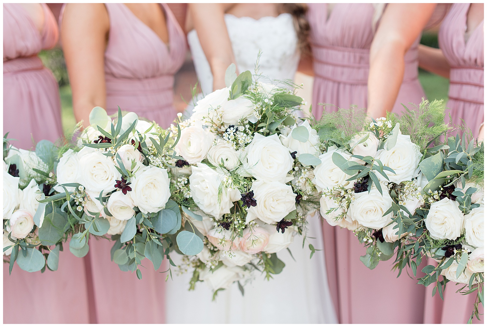 close up of bride with bridesmaids in mauve dresses displaying their bouquets of white flowers and eucalyptus