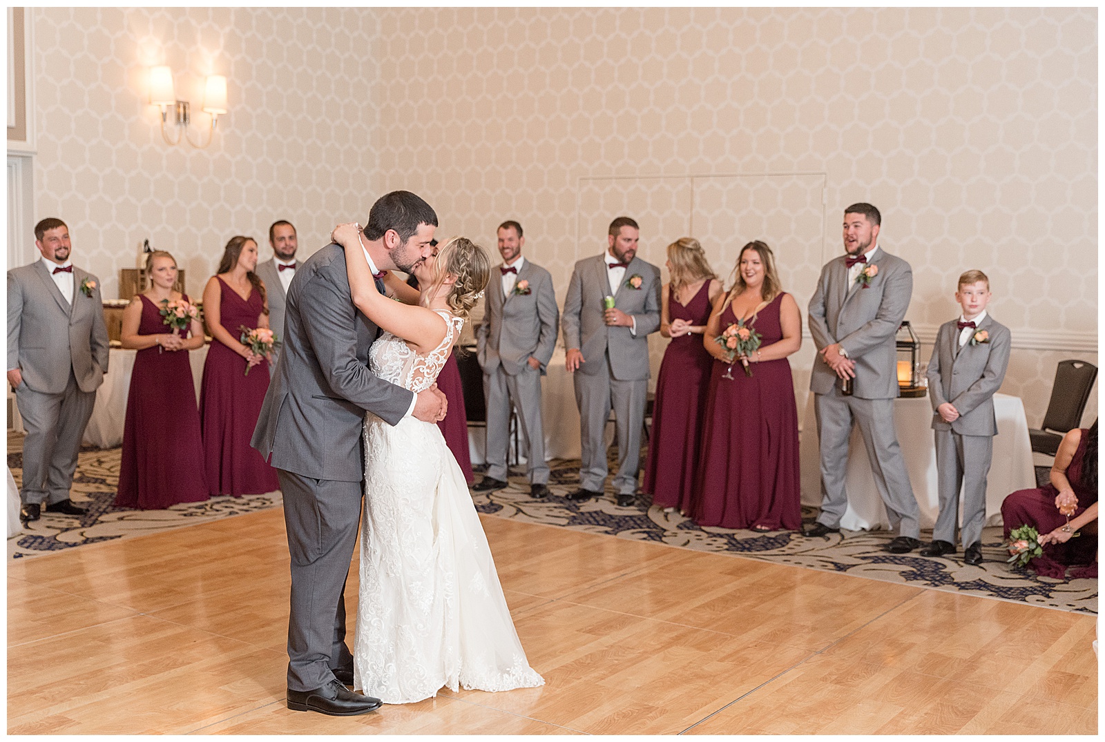 groom and bride hug and kiss during their first dance surrounded by their bridal party