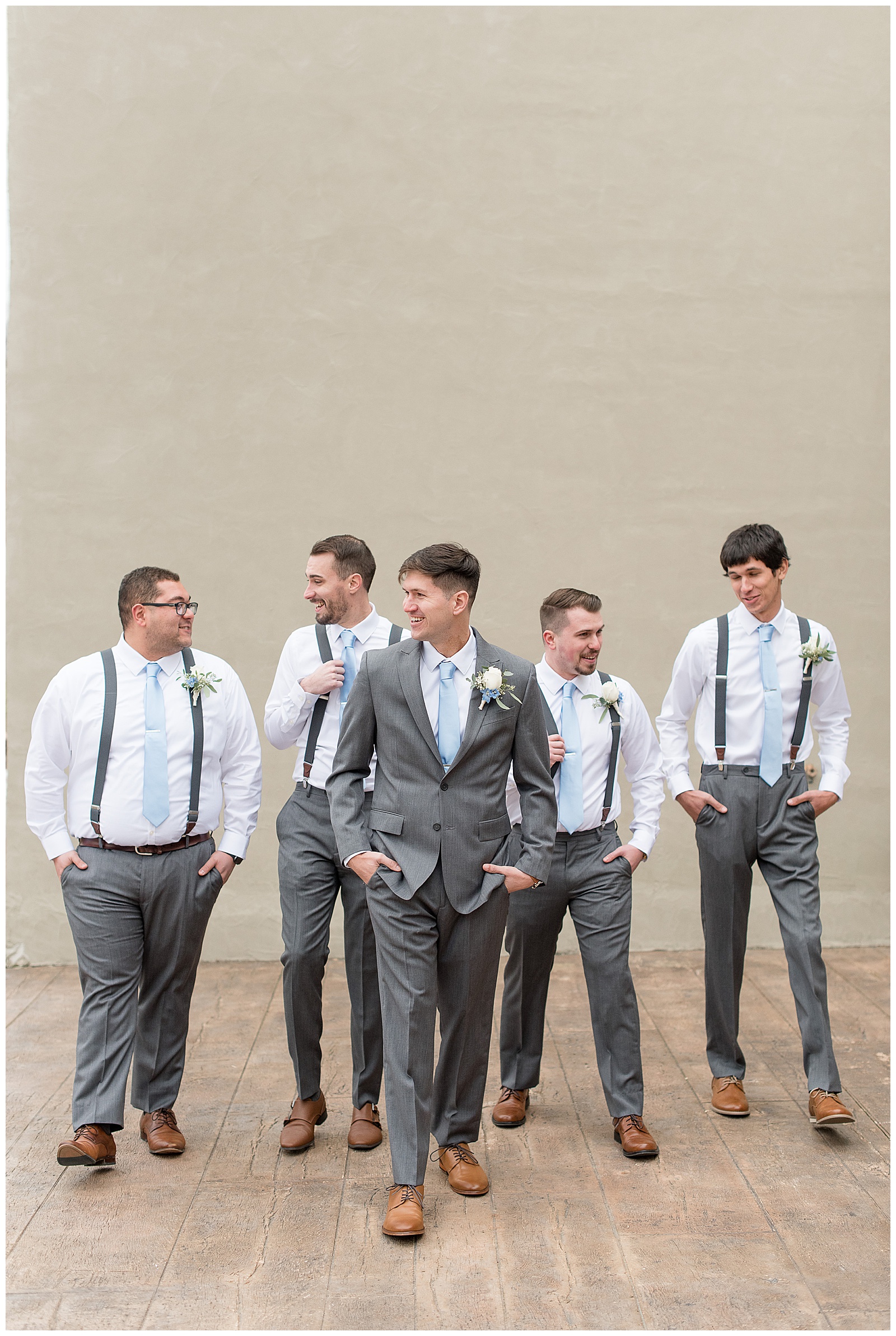 groom walking towards camera with groomsmen also walking behind him with their hands in their pockets all looking at one another smiling