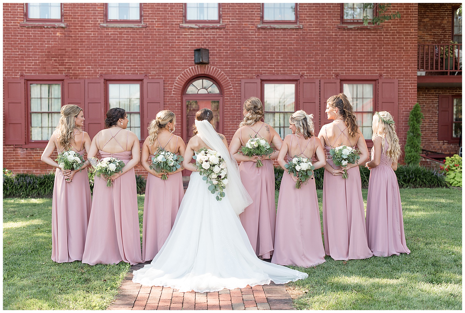 bride with her bridesmaids in mauve gowns all standing backwards with bouquets displayed behind their backs at the country barn