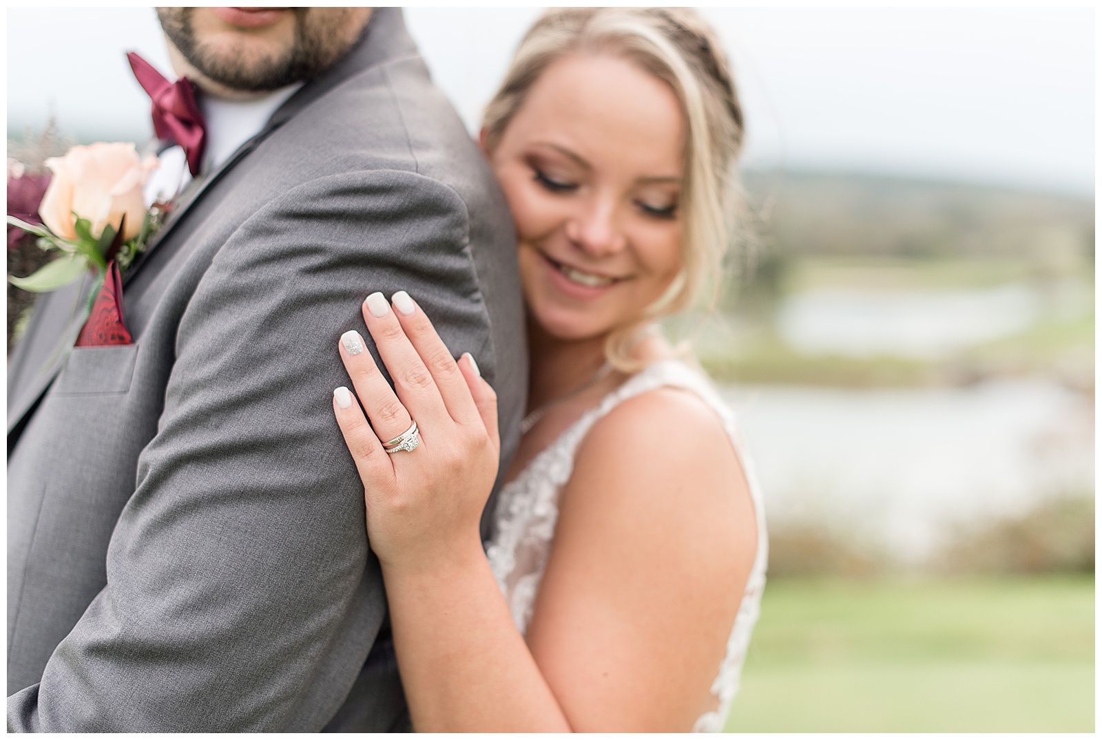bride hugging her groom from behind smiling and looking down displaying her wedding ring on his arm