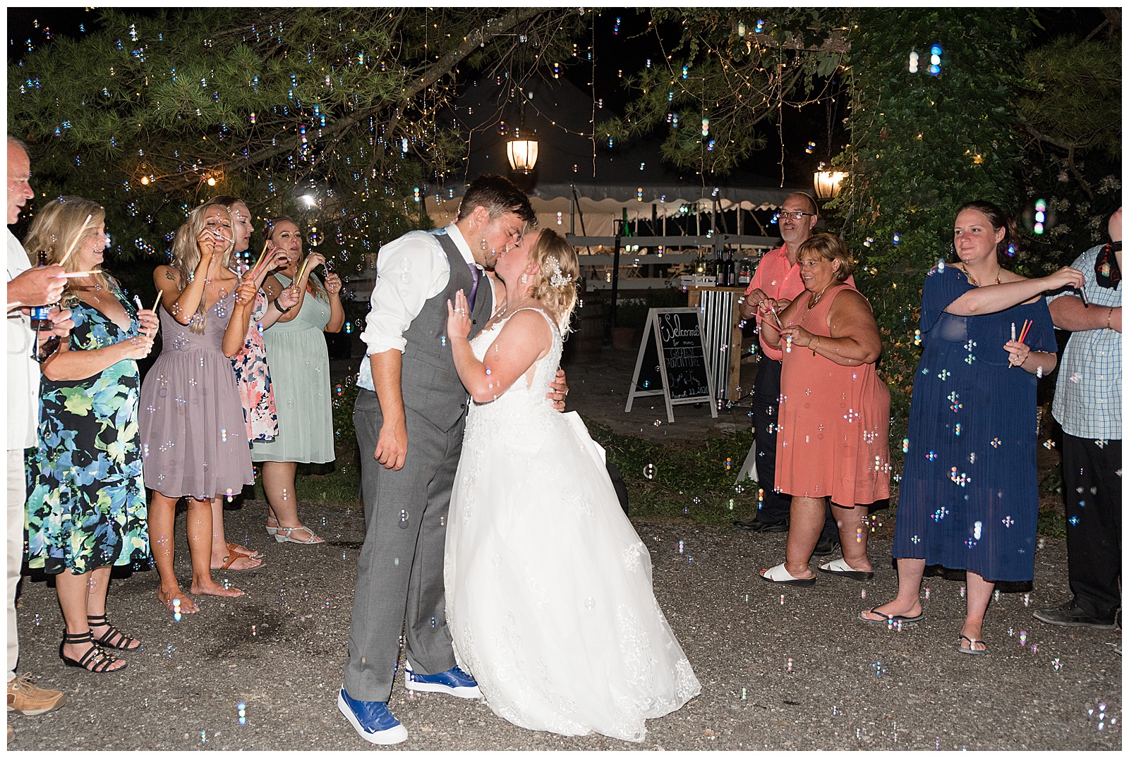 groom hugging and kissing his bride while dancing at reception in the dark surrounded by guests and bubbles
