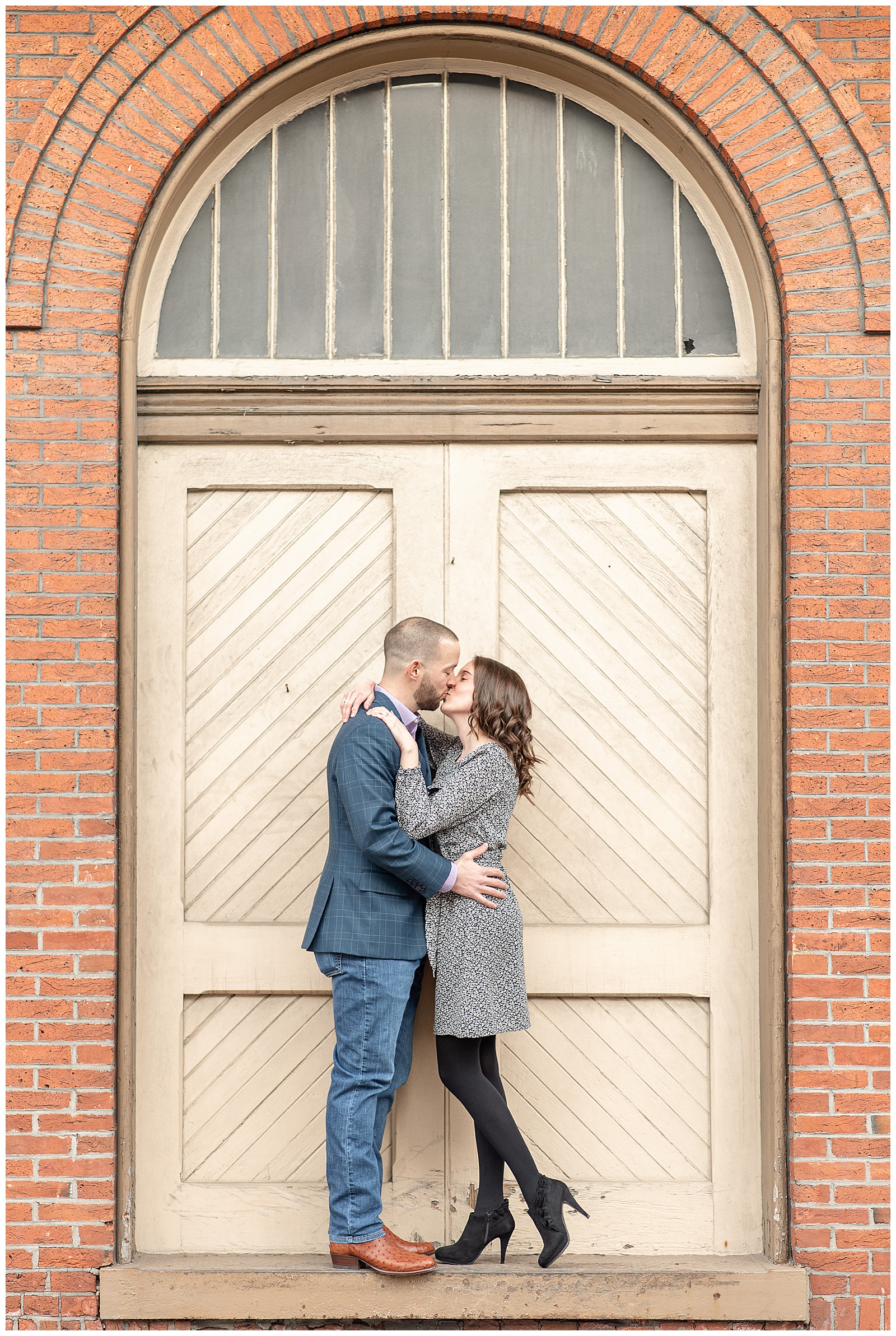 couple kissing in front of cream archway door in brick building at Ellicott City
