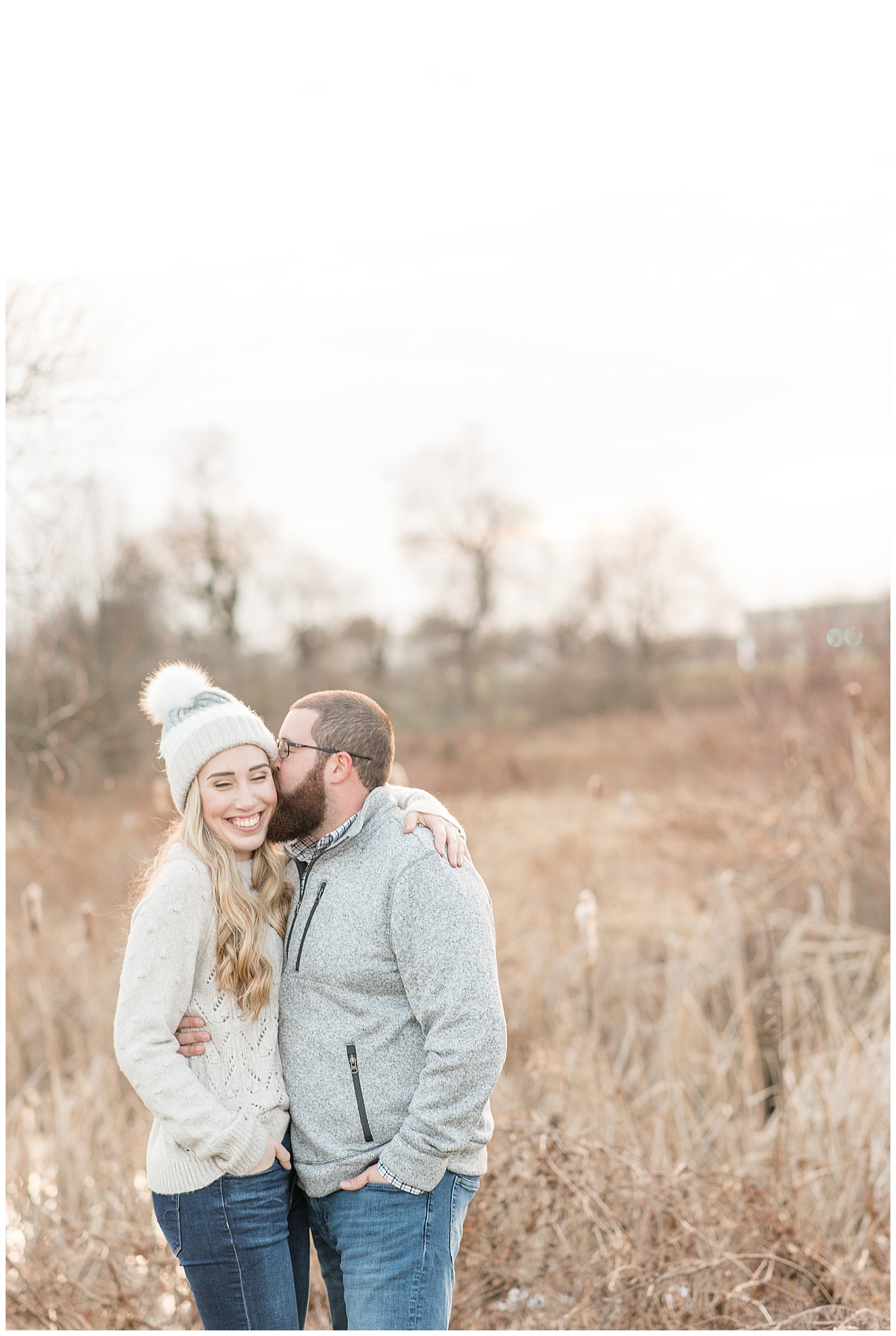 winter engagement session with girl wearing snow hat and guy giving her a kiss on the cheek
