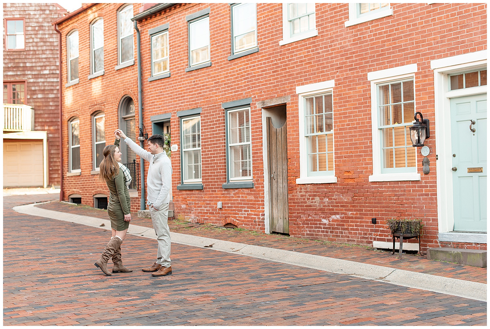 couple twirling in middle of cobblestone road with brick buildings on either side