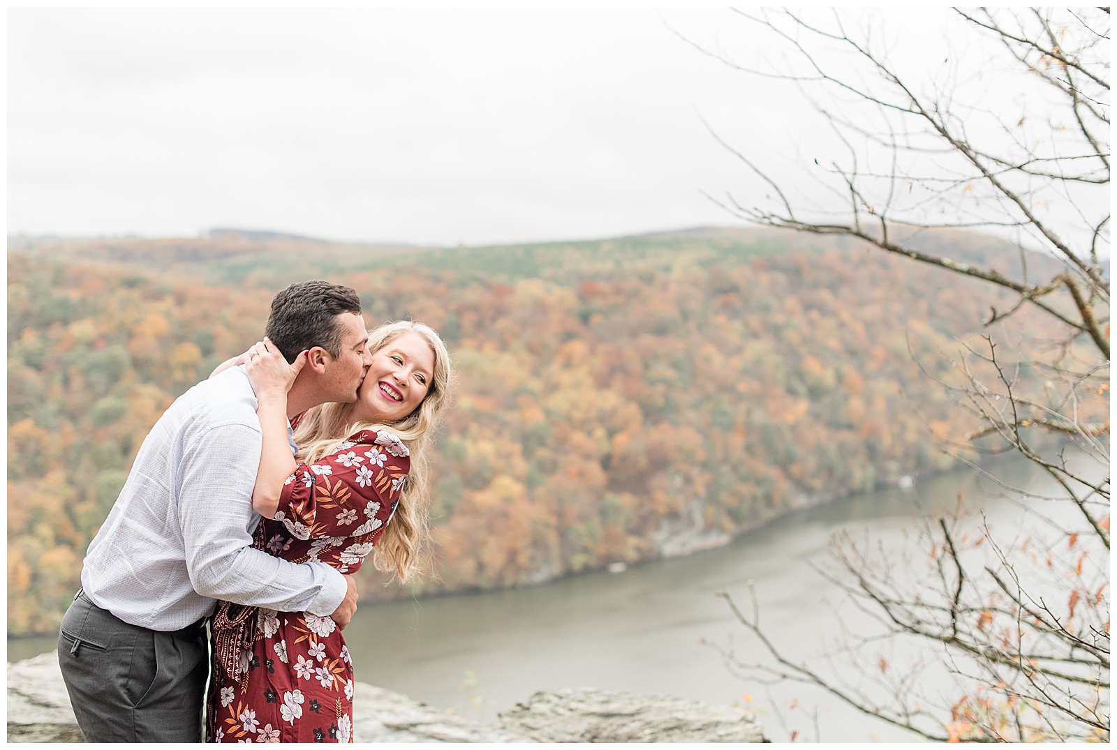 couple standing on rock overlooking Susquehanna River with guy kissing her on the cheek