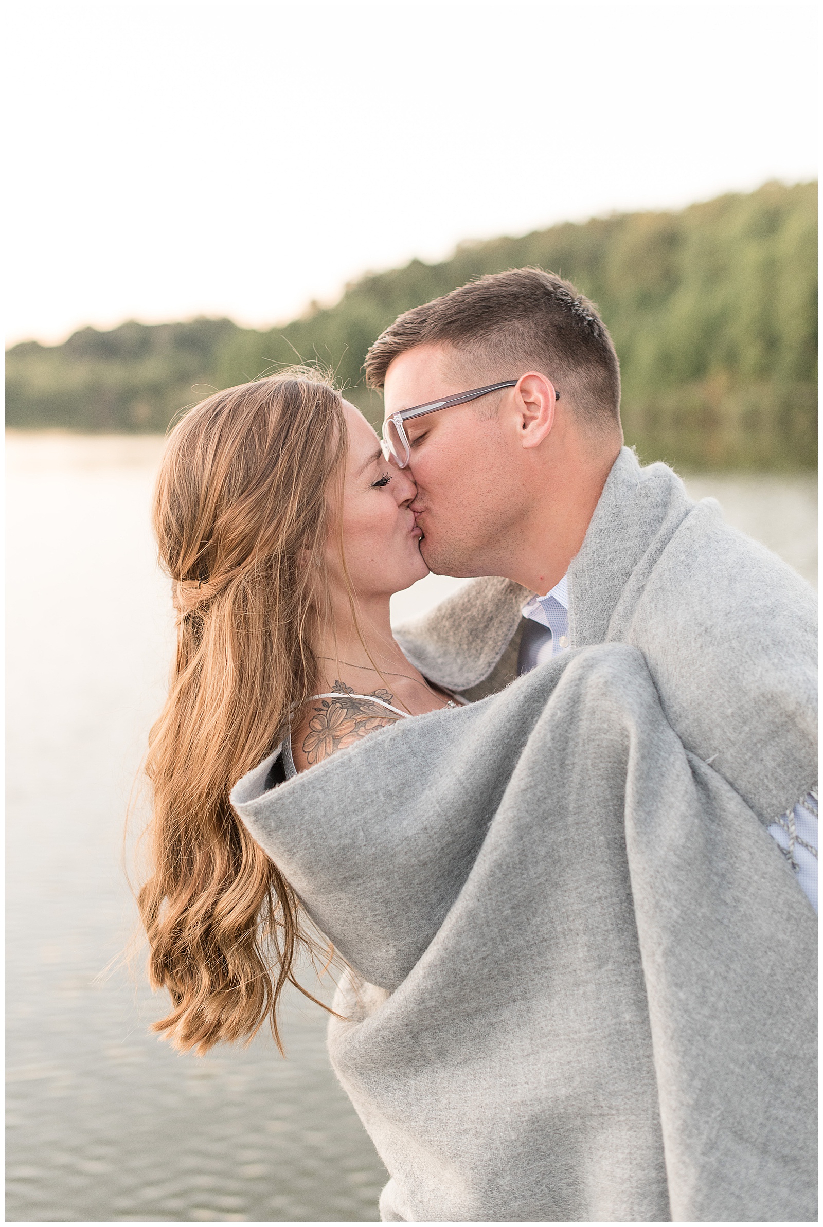 couple kissing in front of lake wrapped up in blanket