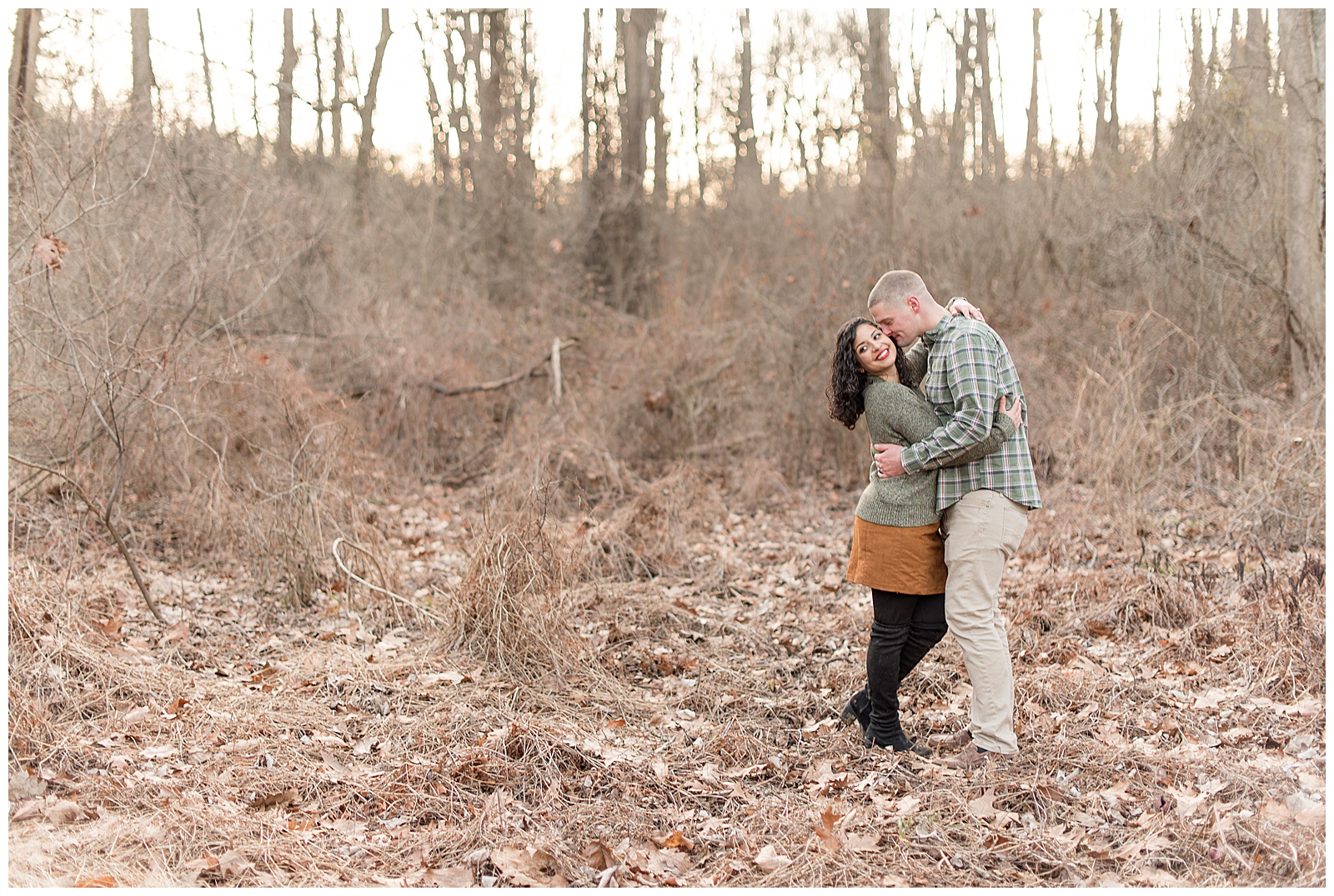 engaged couple standing in wooded area during winter all wrapped up
