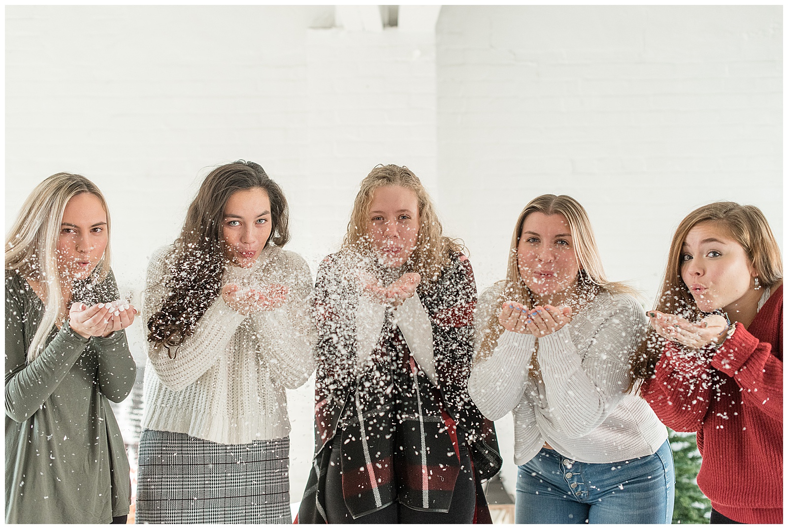 girls standing close blowing fake snow out of their cupped hands towards the camera at hingeworks