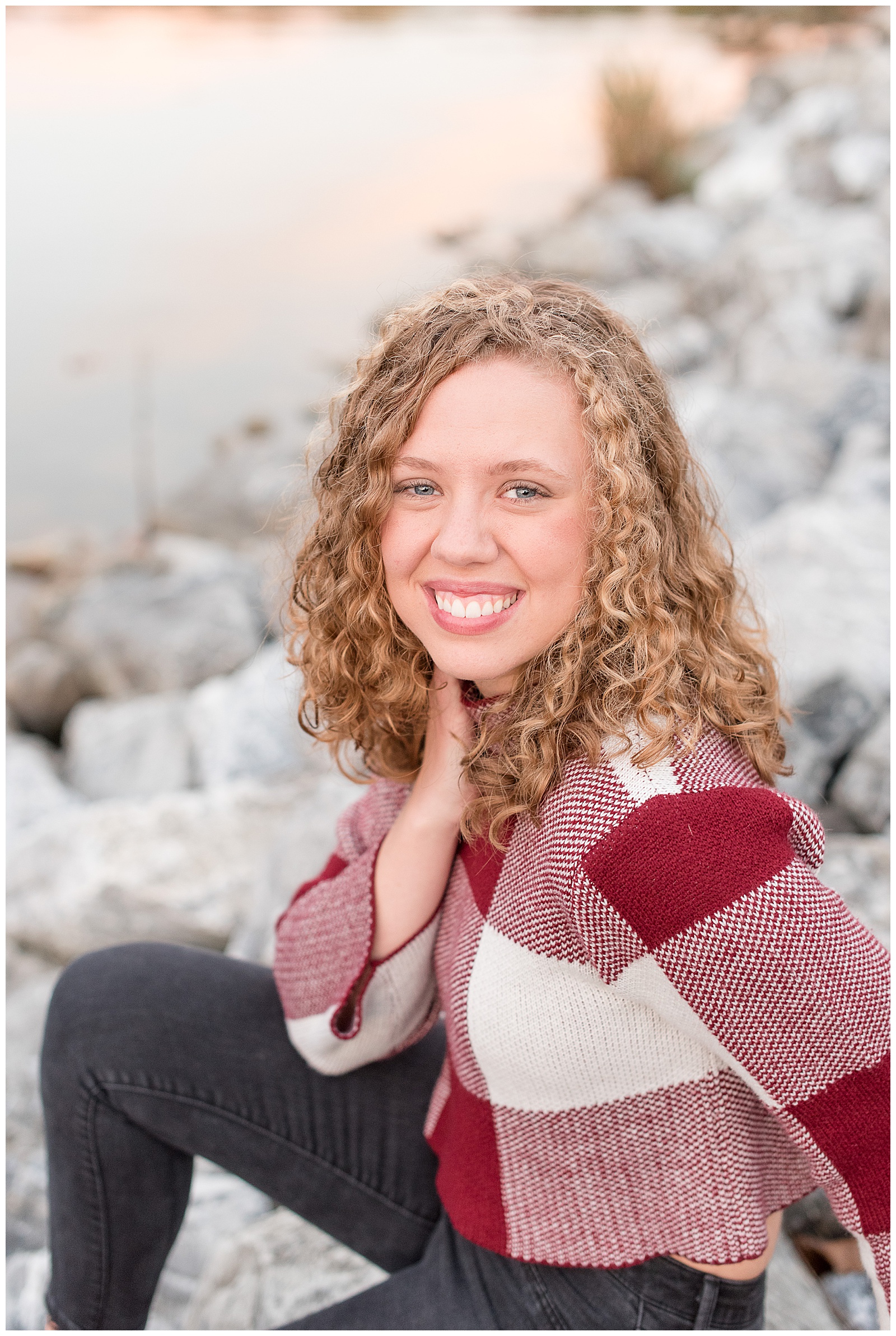 senior girl sitting along rocky bank smiling at camera by lake in lancaster pennsylvania