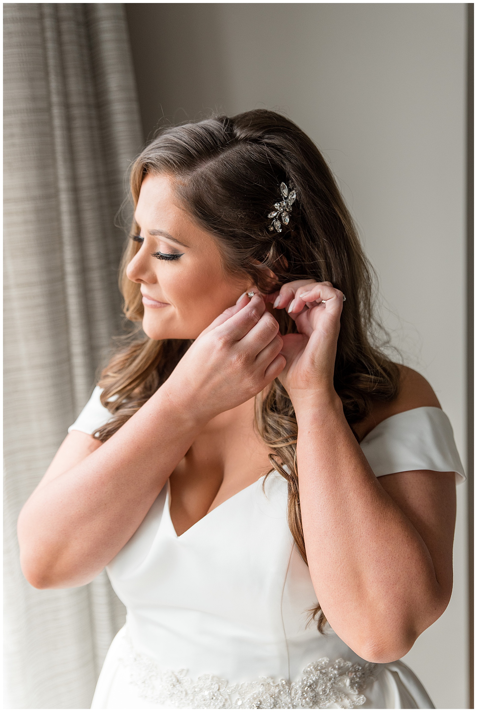 bride putting left earring in wearing white off the shoulder bridal gown in downtown lancaster pennsylvania