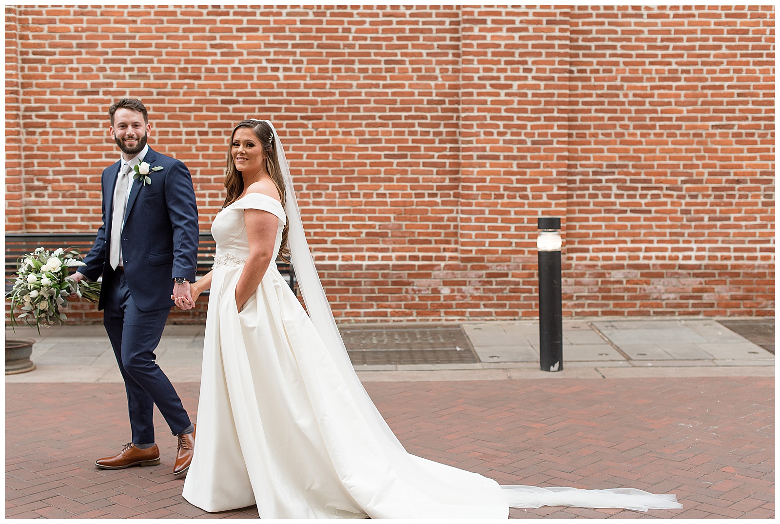 groom holding bride's hand as he leads her walking past camera by brick wall in lancaster pennsylvania
