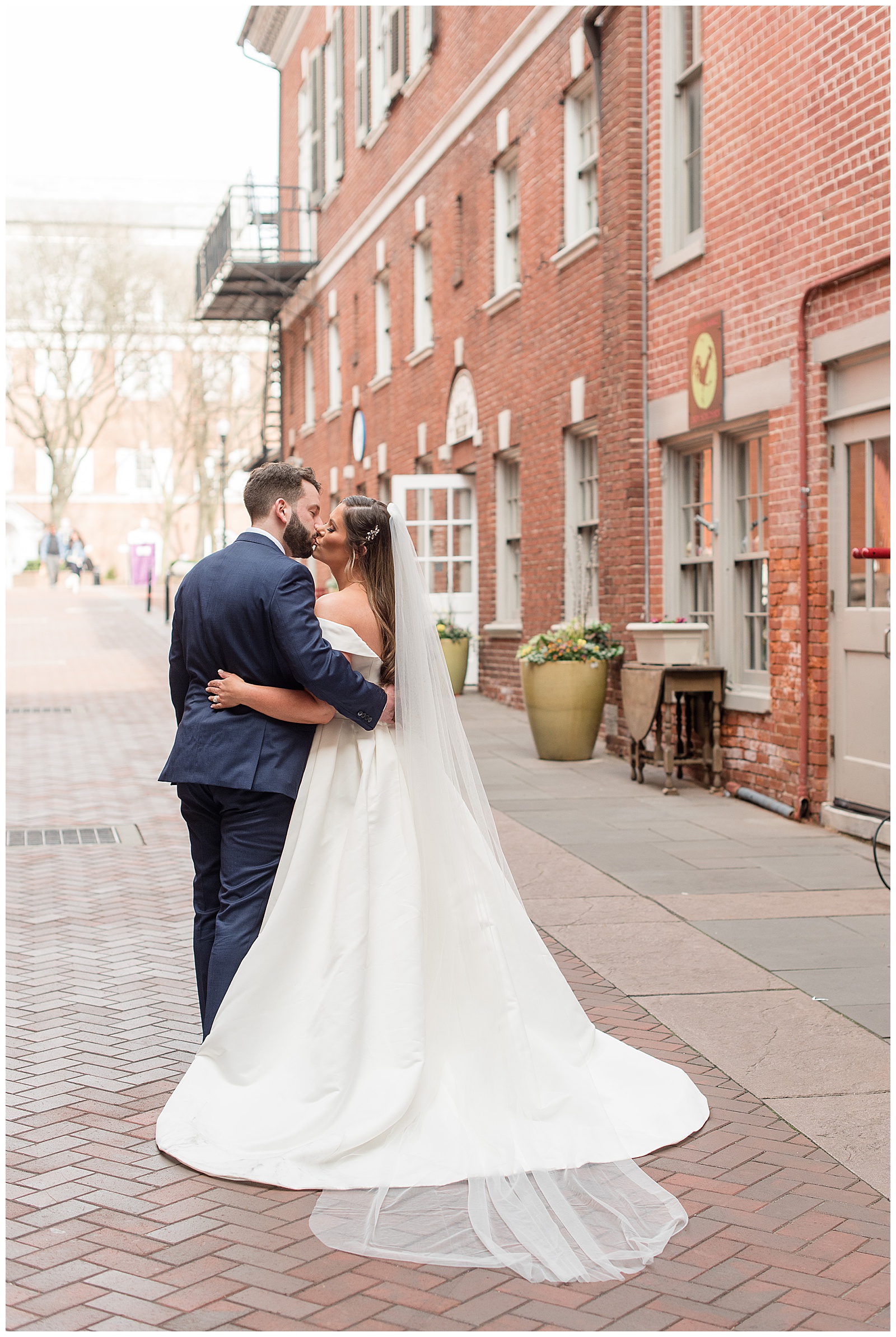 groom and bride standing close kissing with their backs to camera on cobblestone street in downtown lancaster pennsylvania