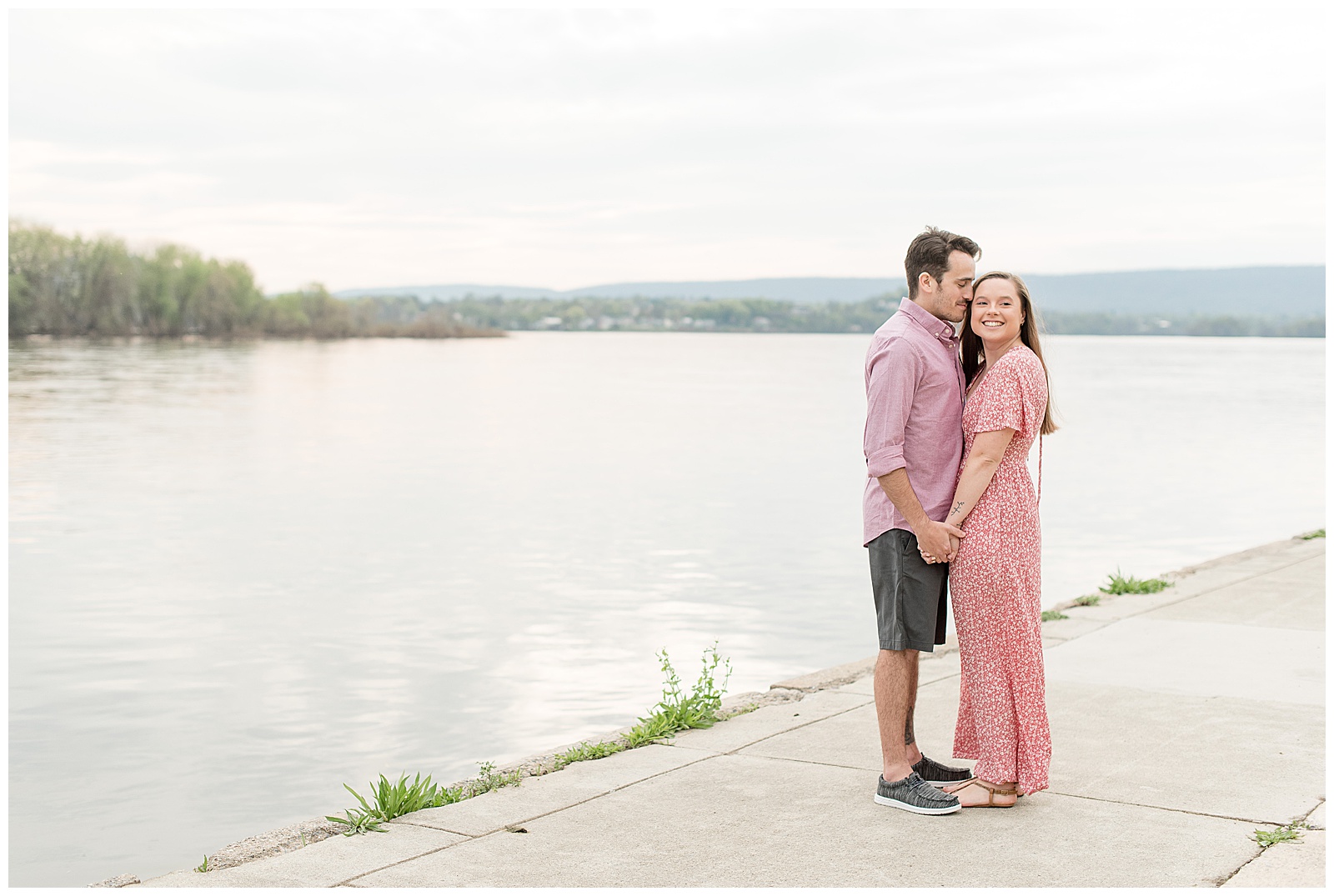 couple standing close along susquehanna river with guy rest head on girl as she smiles at camera