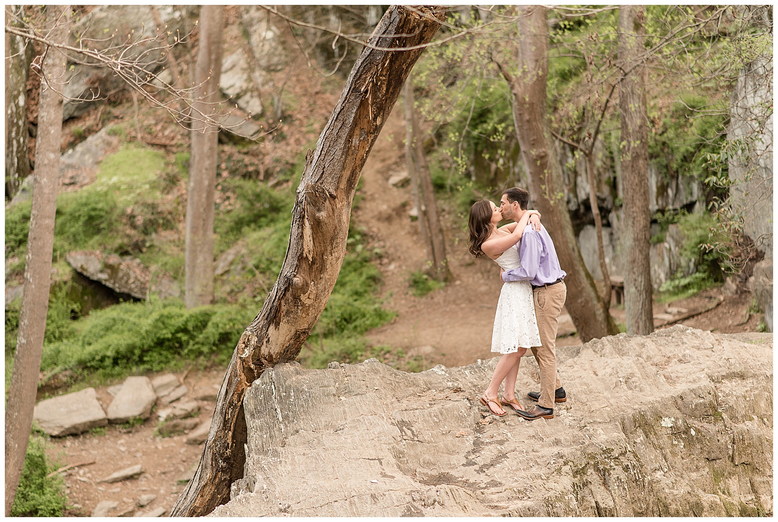 guy dips girl back as he kisses her on large rock with tree growing crooked beside them at rocks state park