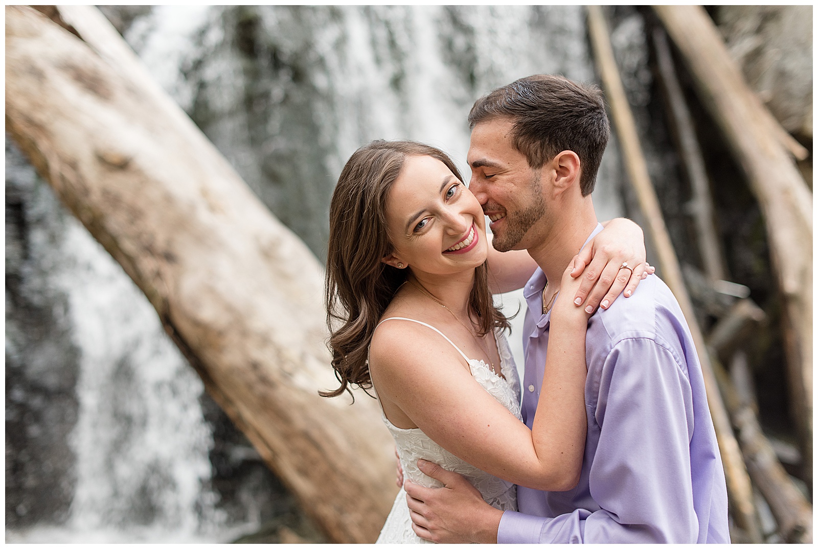 couple hugging tightly as girl smiles at camera and guy rests his nose against her left cheek by kilgore falls