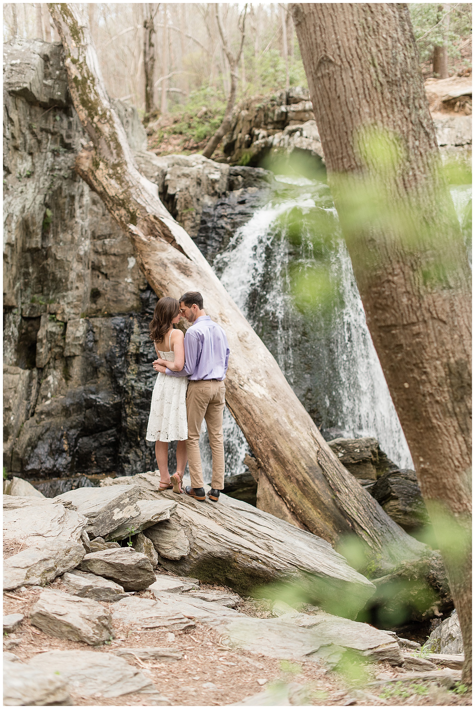 couple hugging with backs toward camera standing on large rock by kilgore falls in northern maryland