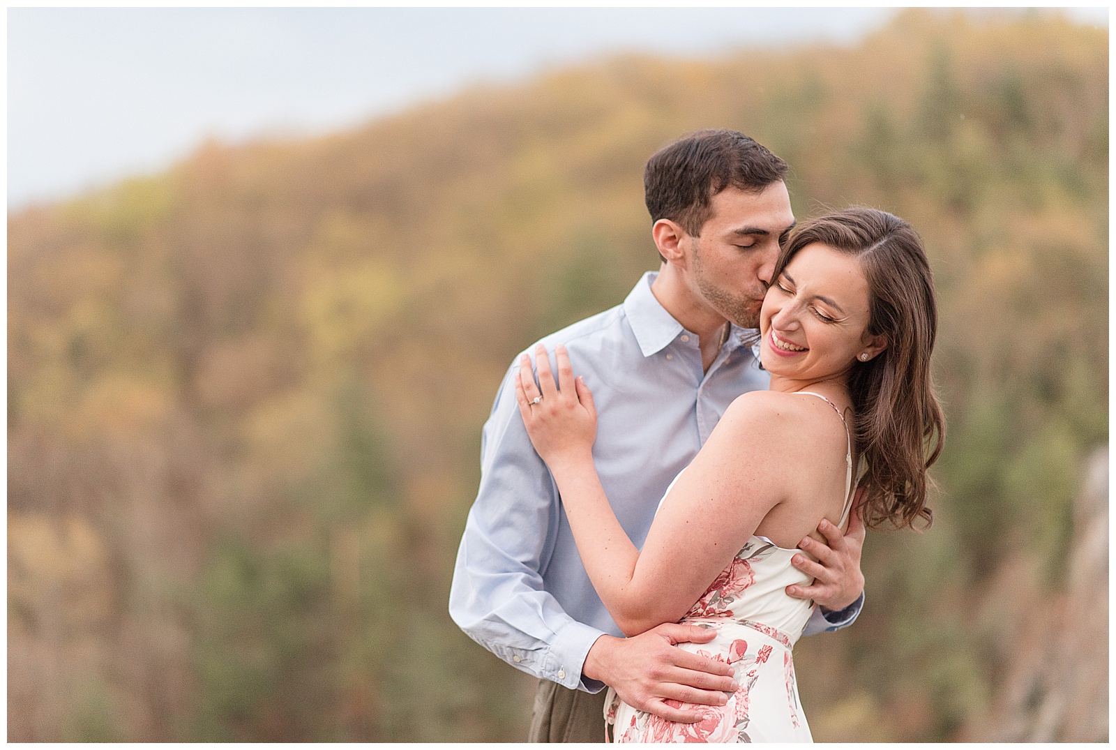 guy kissing girl's right temple as she smiles and looks down with forest behind them at rocks state park