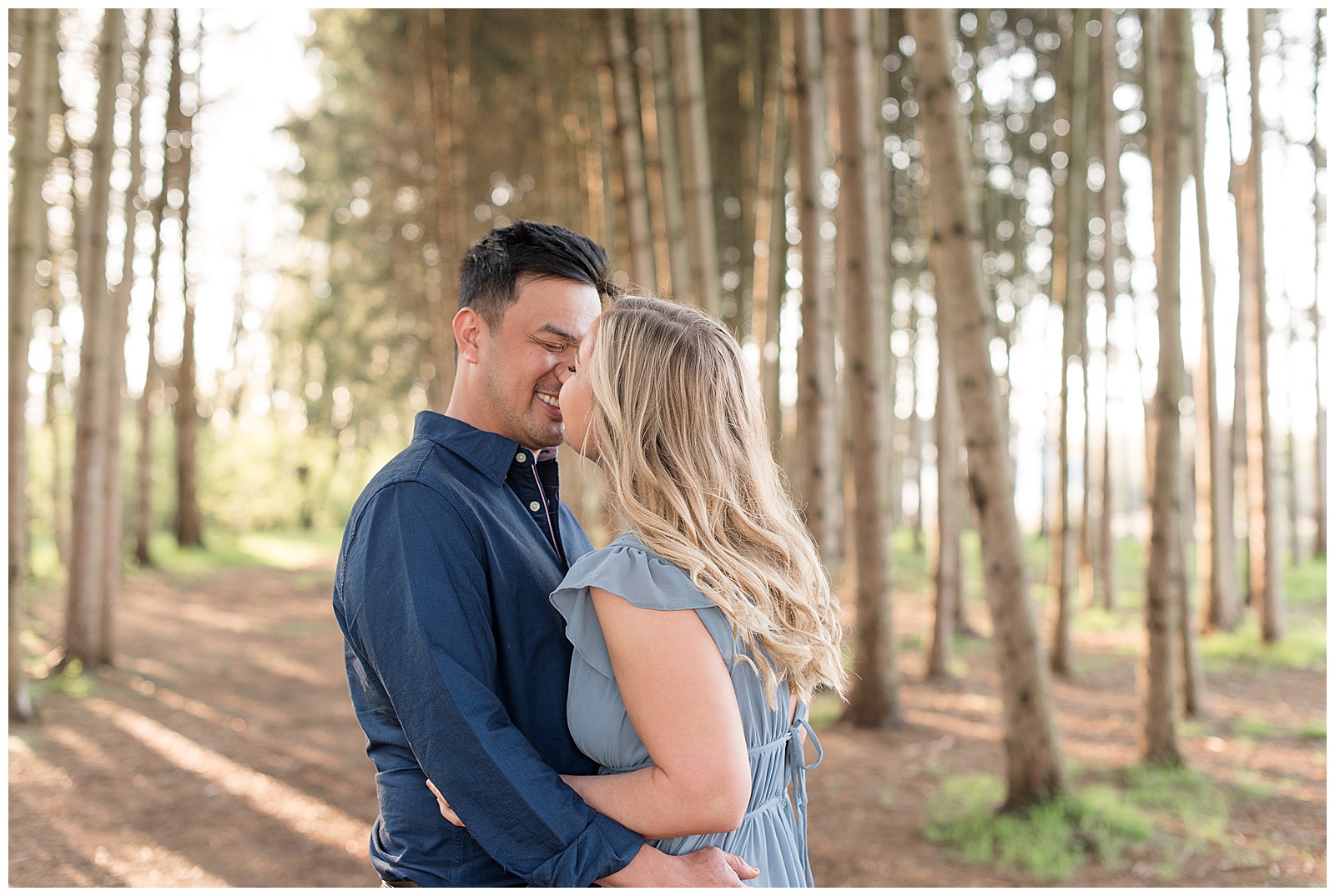 couple almost kissing while hugging by row of pine trees at overlook park