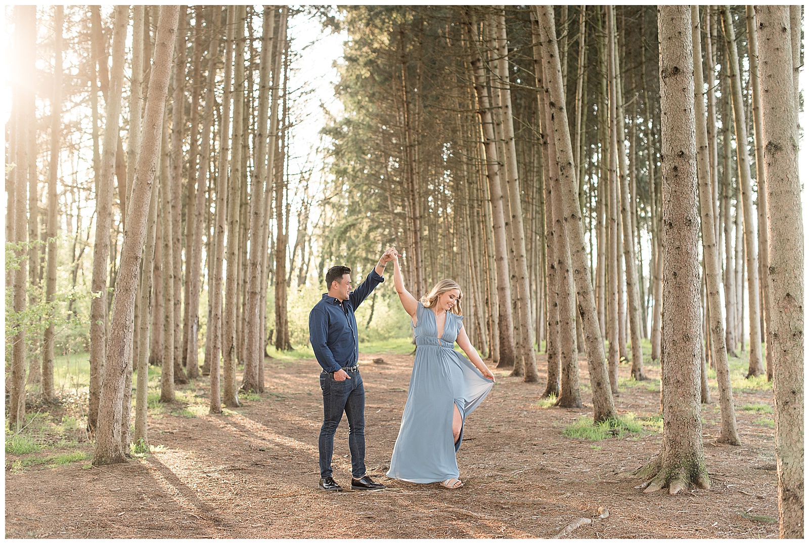 guy twirling girl who's wearing light blue flowy dress in between grove of pine trees in lancaster pennsylvania