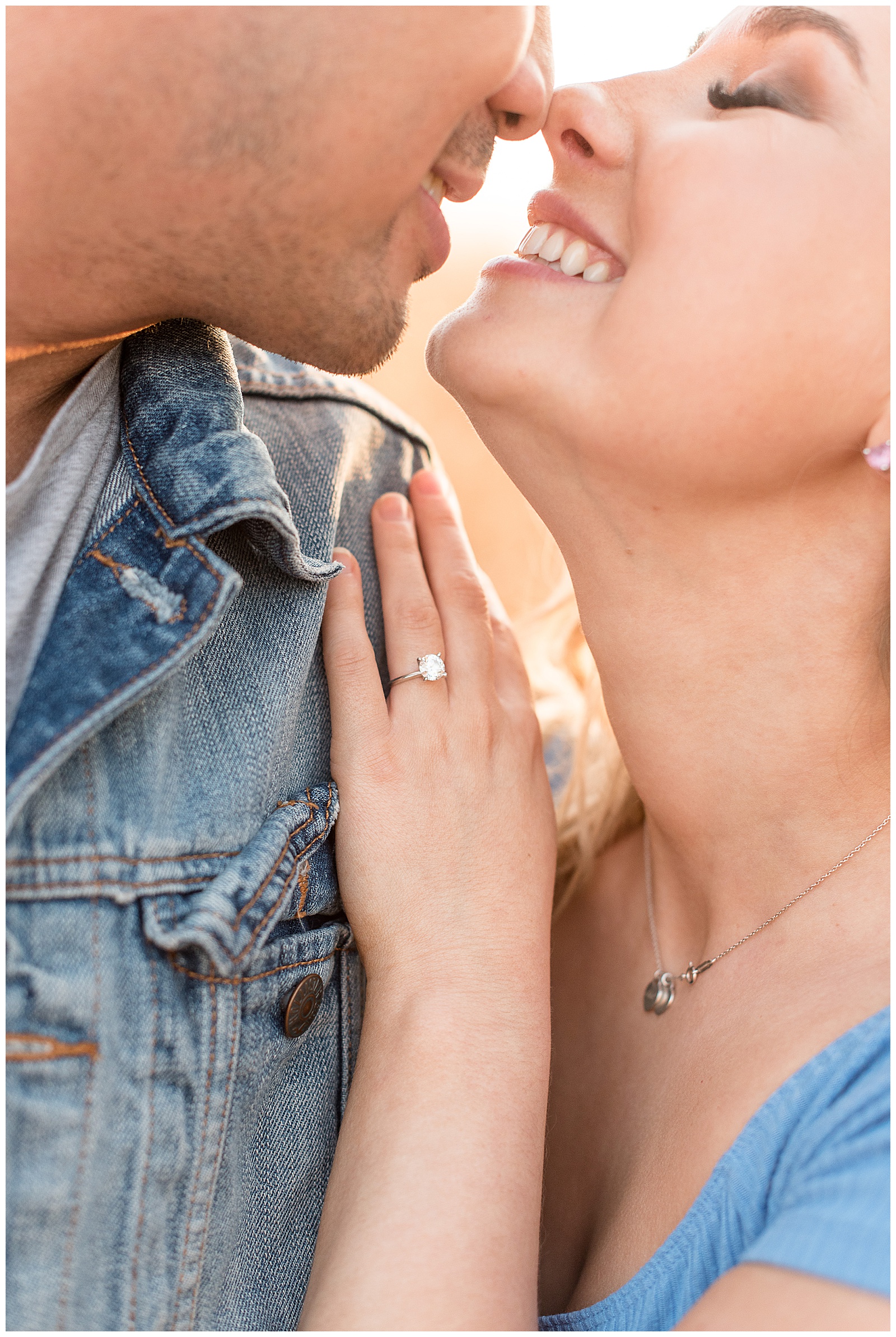 close up of engagement ring resting on guy's shoulder as couple smiles and almost kisses
