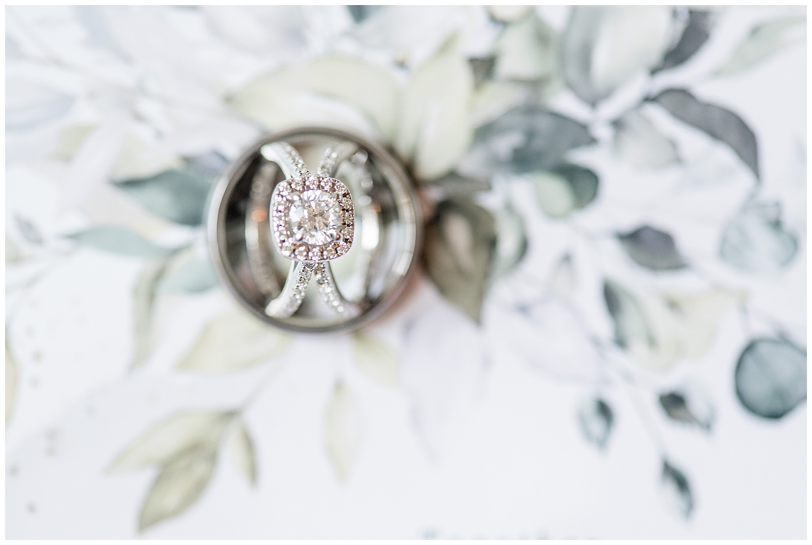 diamond engagement and wedding rings resting inside groom's wedding band on top of floral backdrop