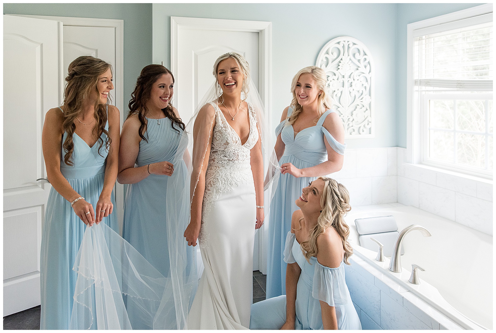 bridal in sleeveless white dress surrounded by bridesmaids in light blue dresses in bridal suite
