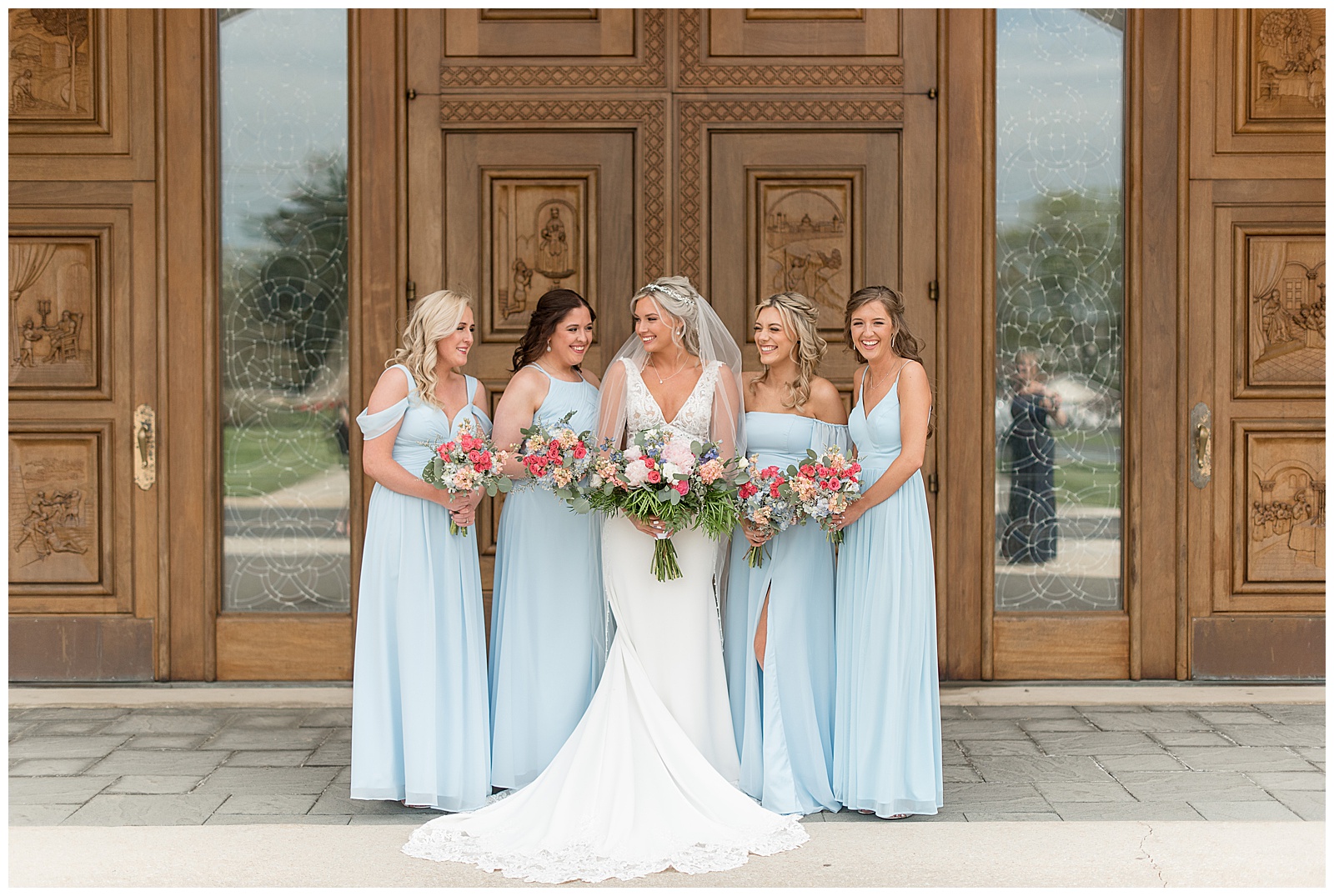 bride surrounded by bridesmaids all holding their spring bouquets and looking at each other by wooden door in maryland