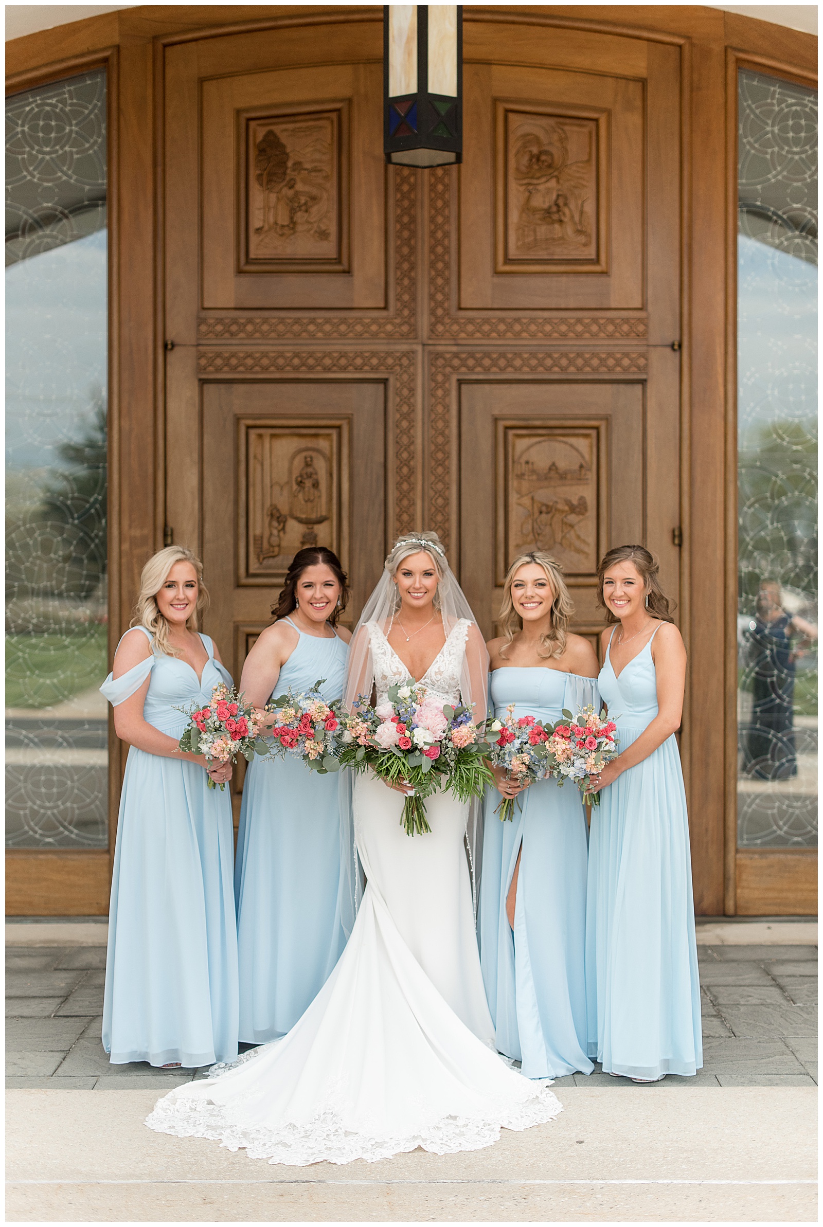 bride surrounded by four bridesmaids wearing light blue dresses and all smiling and looking at camera while holding bouquets