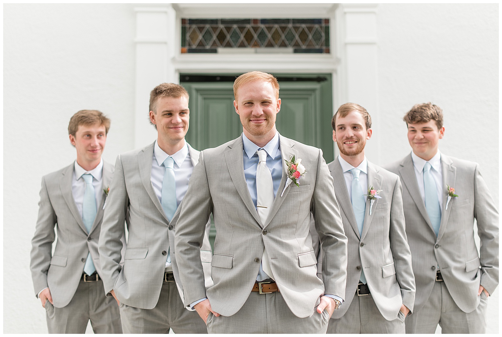 groom walking ahead of four groomsmen all wearing light gray suits with hands in their pockets