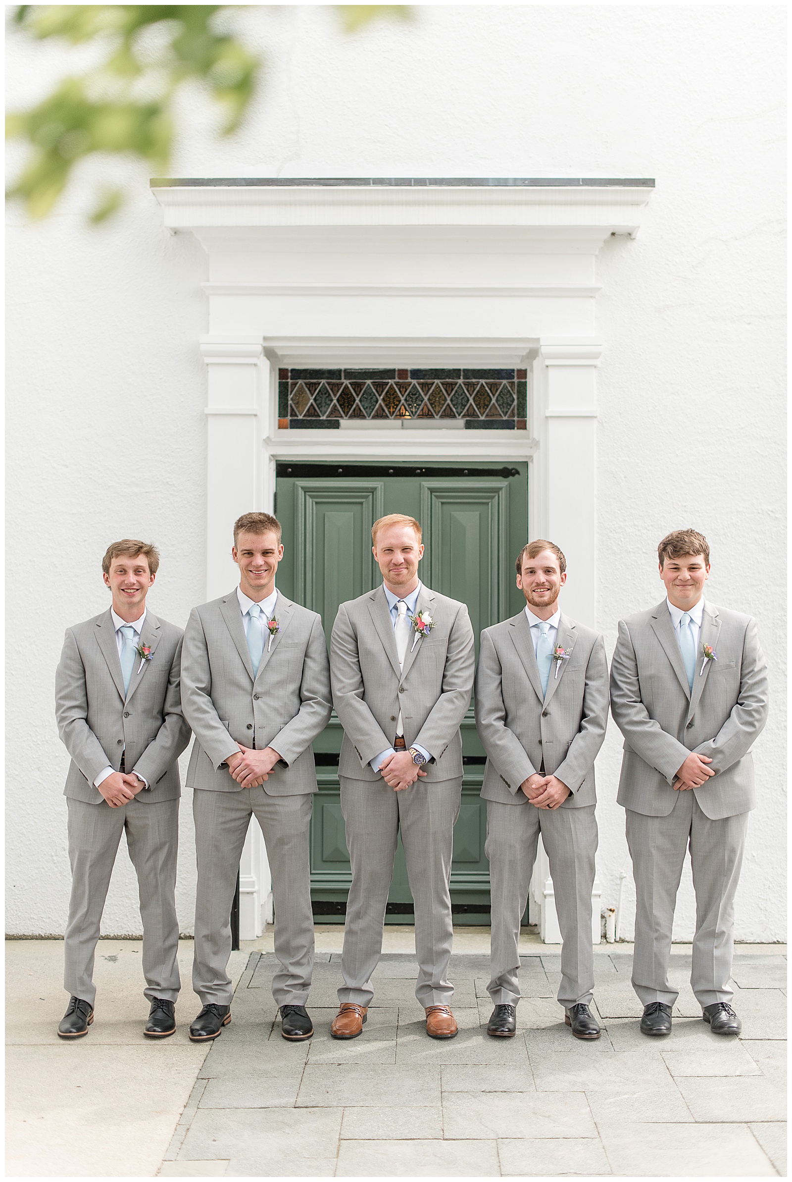 groom surrounded by groomsmen by historic white building with green door in maryland
