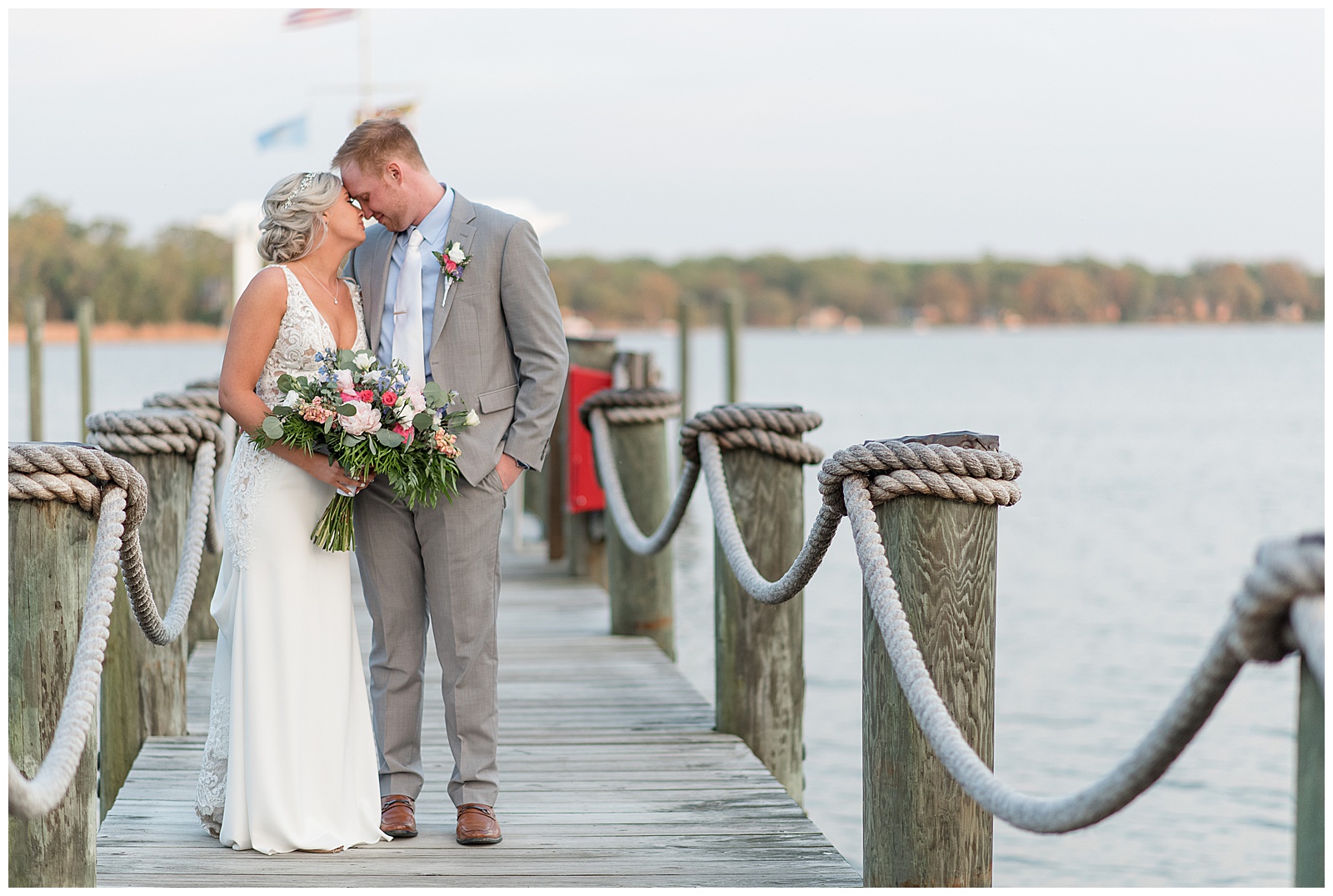 bride holding bouquet and snuggling tightly with groom on beautiful dock along water at water's edge event center