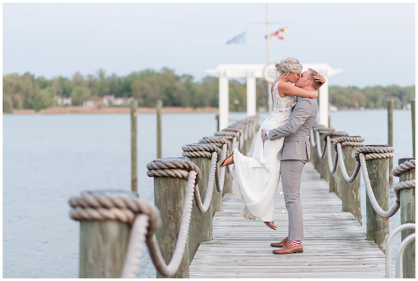 groom lifting bride while kissing on dock at sunset at water's edge event center