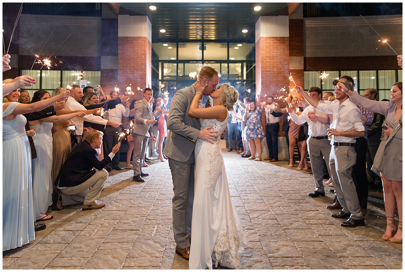 bride and groom kissing surrounded by wedding guests as they leave their reception at water's edge event center