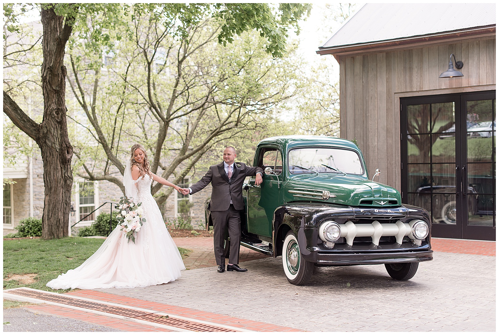 bride smiling holding groom's hand as she pulls away and he leans against vintage pickup truck next to barn