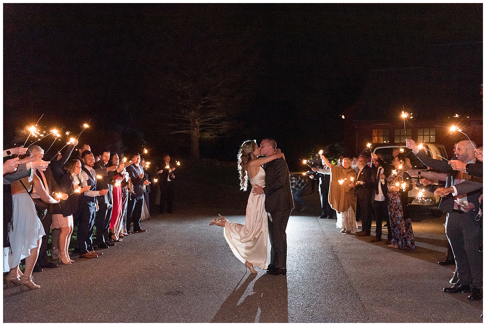 bride and groom kissing in the dark surrounded by their guests holding sparklers and sending them off at the farm at eagles ridge