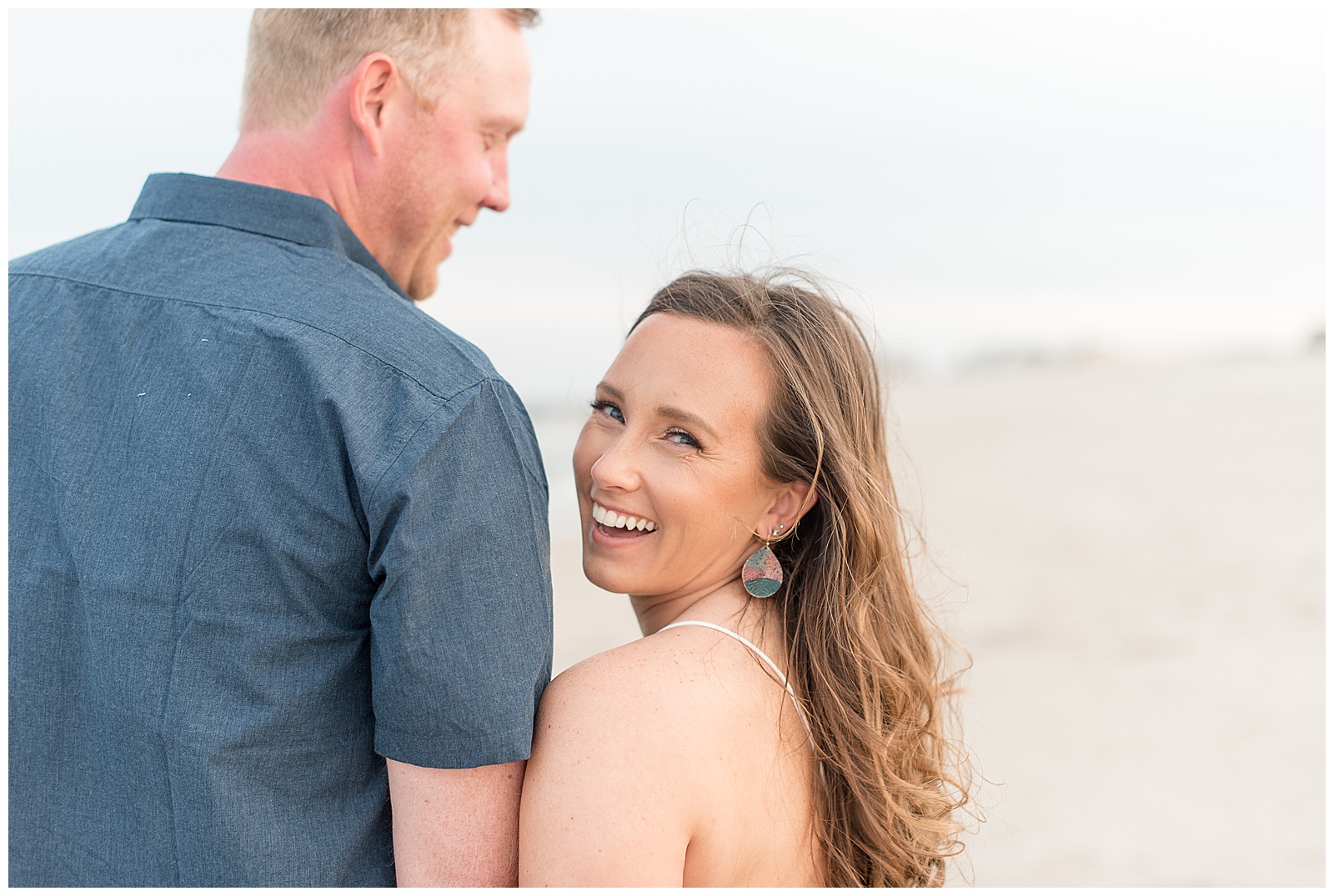 couple on beach as woman looks back over left shoulder smiling at camera and guy smiles at her