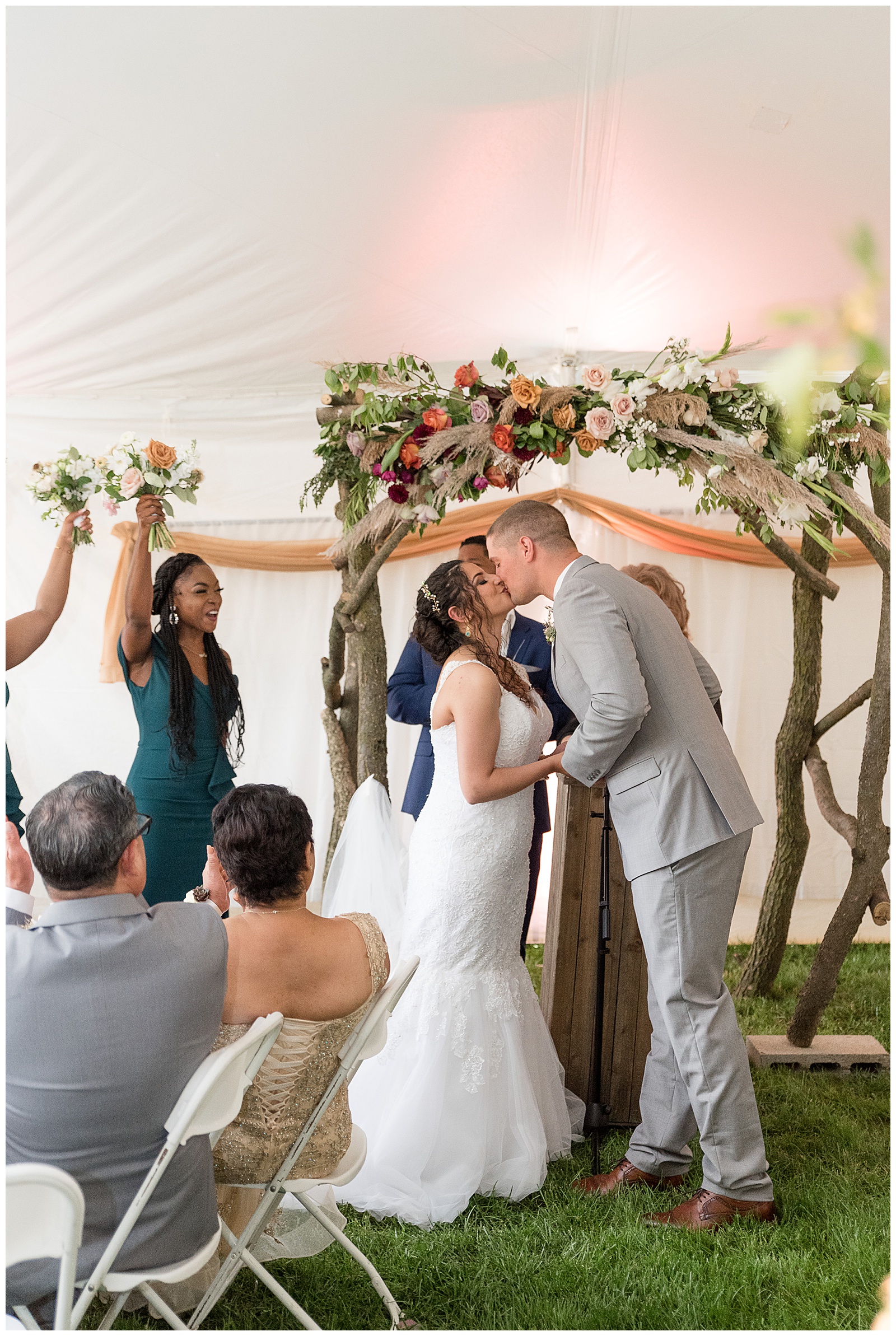 bride and groom kiss inside intimate white tent wedding ceremony as guests cheer
